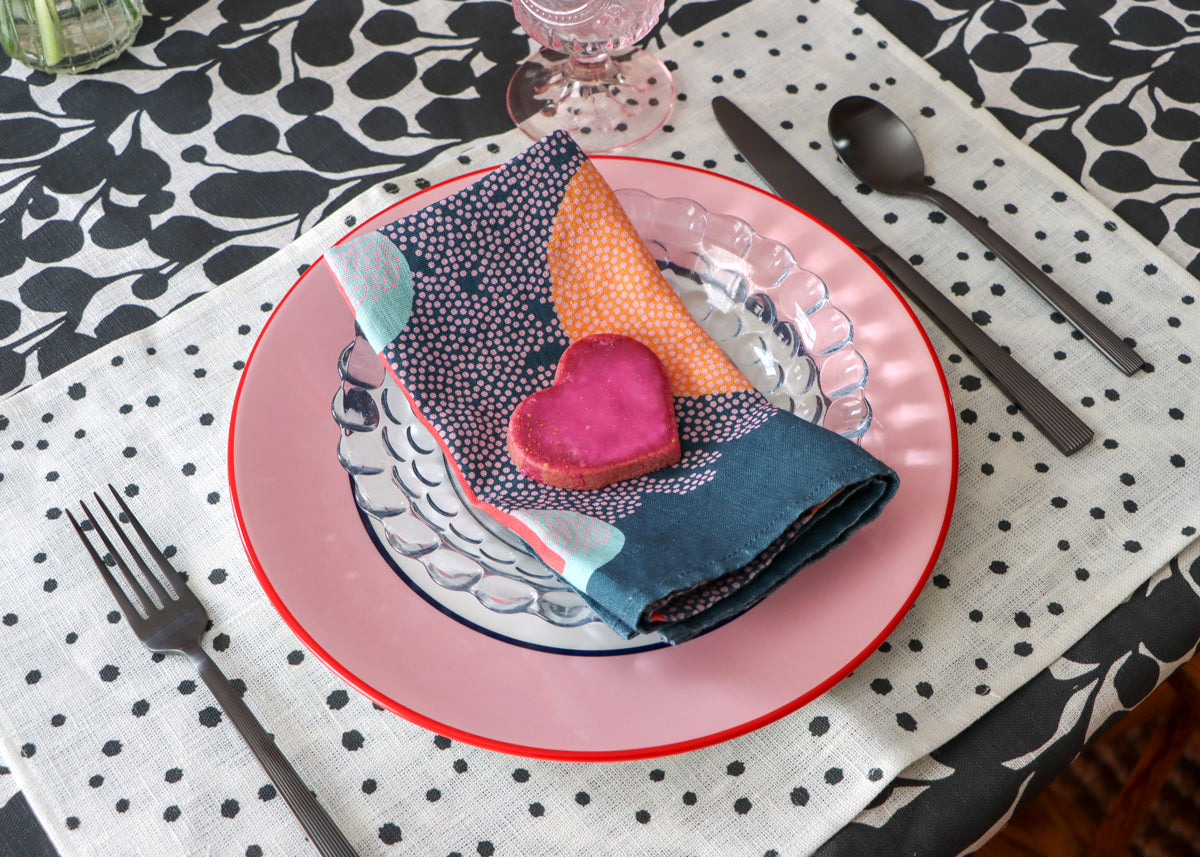 Layered table linens set up for a meal. Blue napkin, black and white dotted placemat, black and white botanical tablecloth, designed by artist Leila Simon Hayes