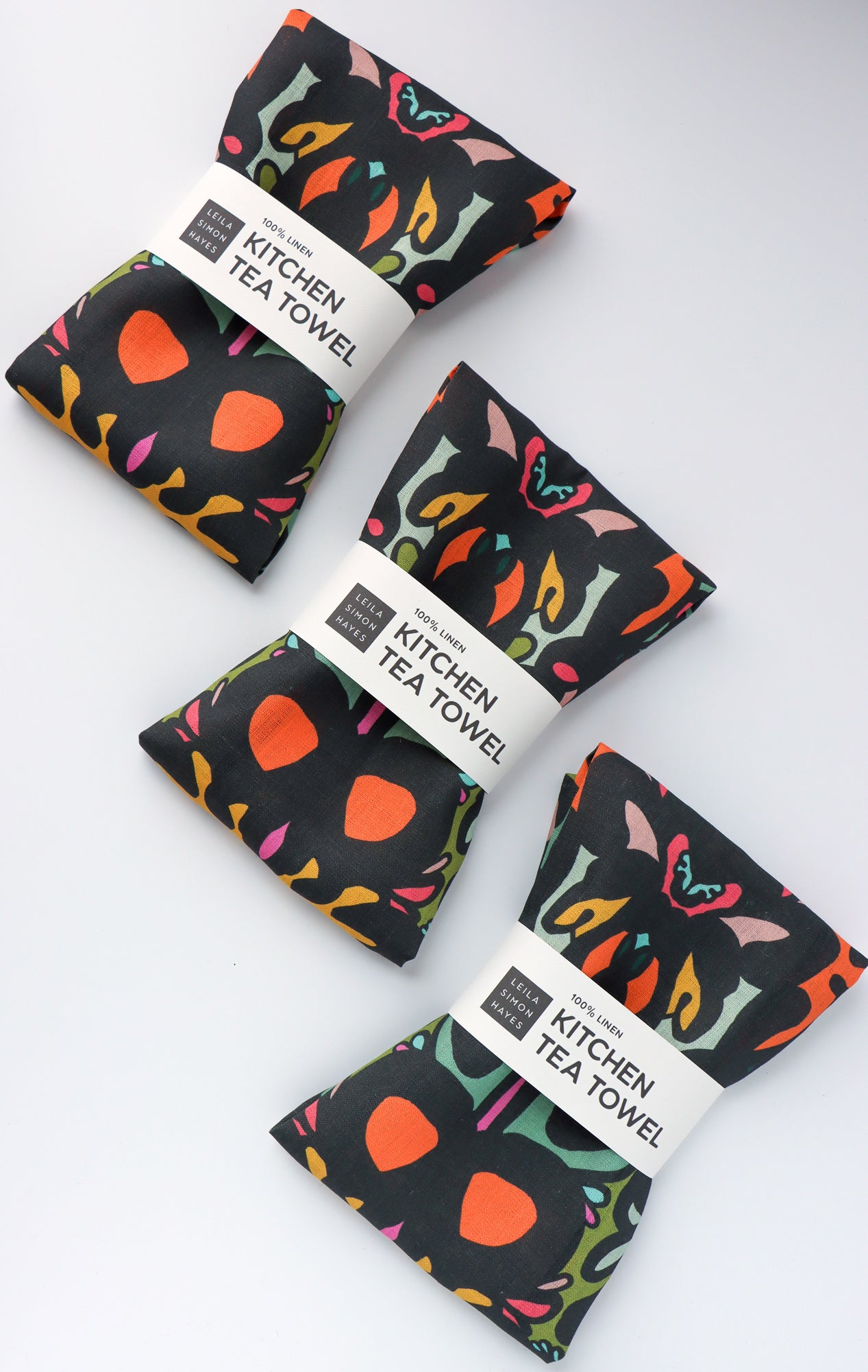 Four kitchen tea towels with colorful designs on a white background. Designed by artist Leila Simon Hayes.