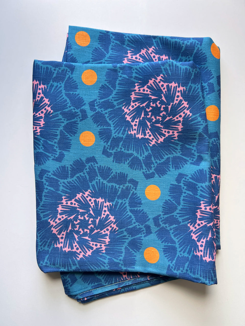 A tablecloth with blue and pink floral patterns and orange dots on a white background designed by artist Leila Simon Hayes