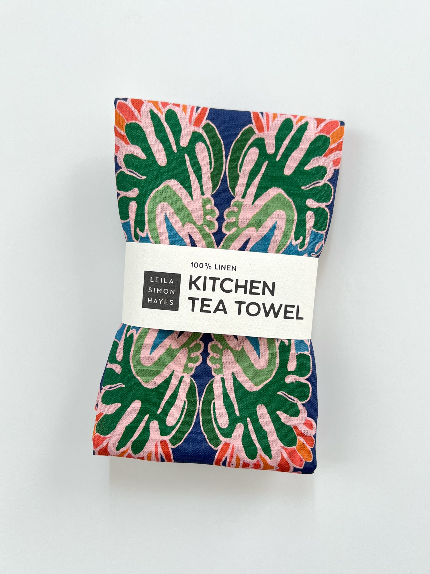 Kitchen tea towel with colorful floral pattern and label saying "100% Linen" on a white background. Designed by artist Leila Simon Hayes.