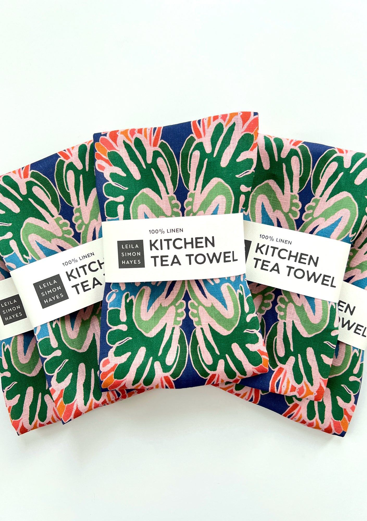 Colorful kitchen tea towels with a pattern and labels saying "100% Linen" on a white background. Designed by artist Leila Simon Hayes.