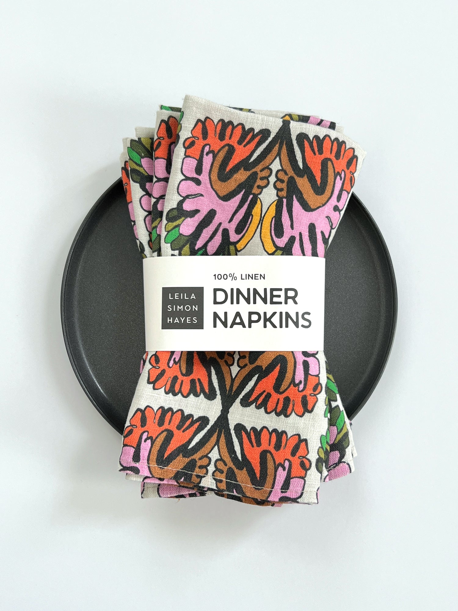 Pack of colorful dinner napkins with a brand label that reads "100% Linen Dinner napkins" designed by artists Leila Simon Hayes on a white background