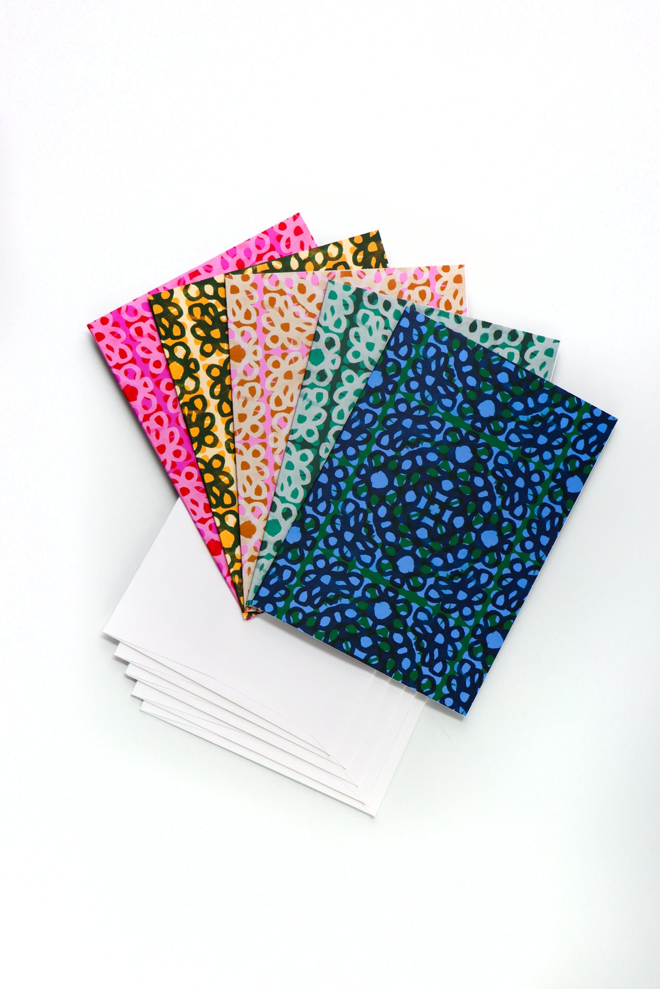 Set of five floral loop patterned folded cards in different colors with envelopes on a white background. Designed by artist Leila Simon Hayes.