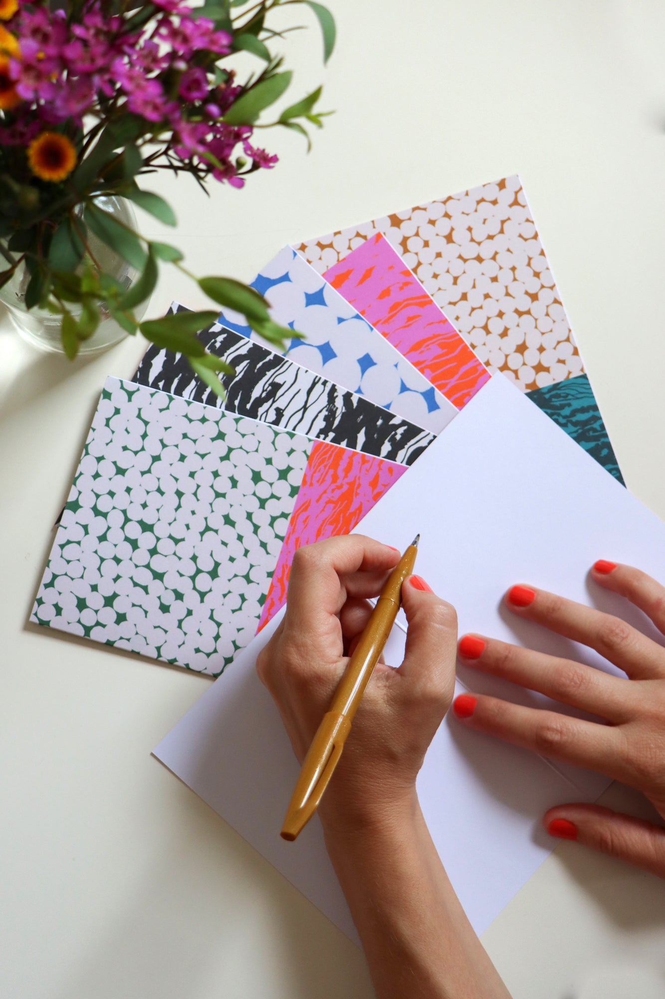 Person writing on the inside of a folded card with colorful folded cards in the background. Designed by artist Leila Simon Hayes.