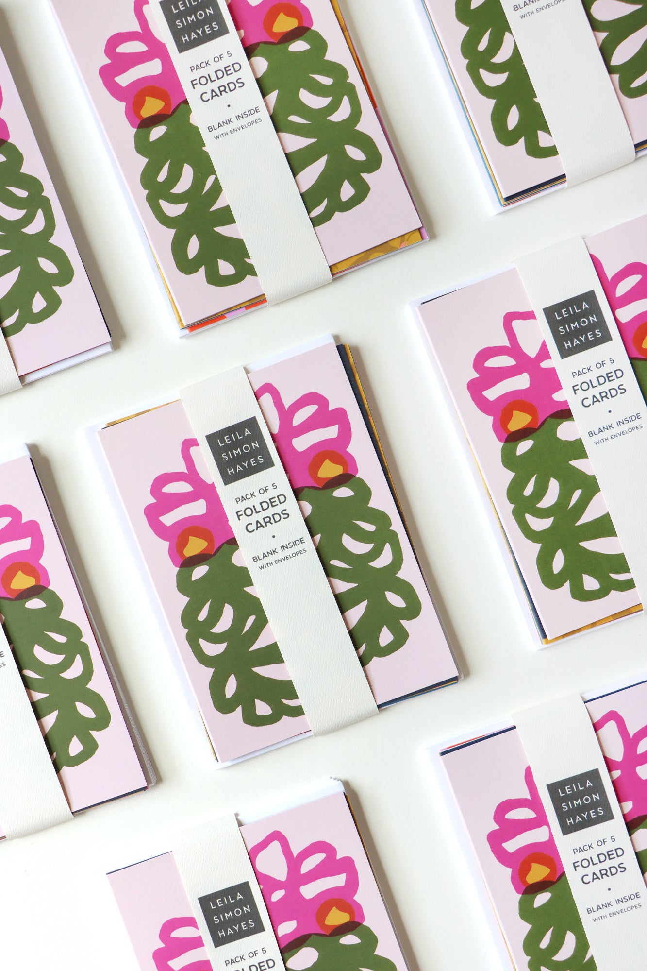 Packaging of folded cards with pink and green floral designs on a white background, designed by artist Leila Simon Hayes.
