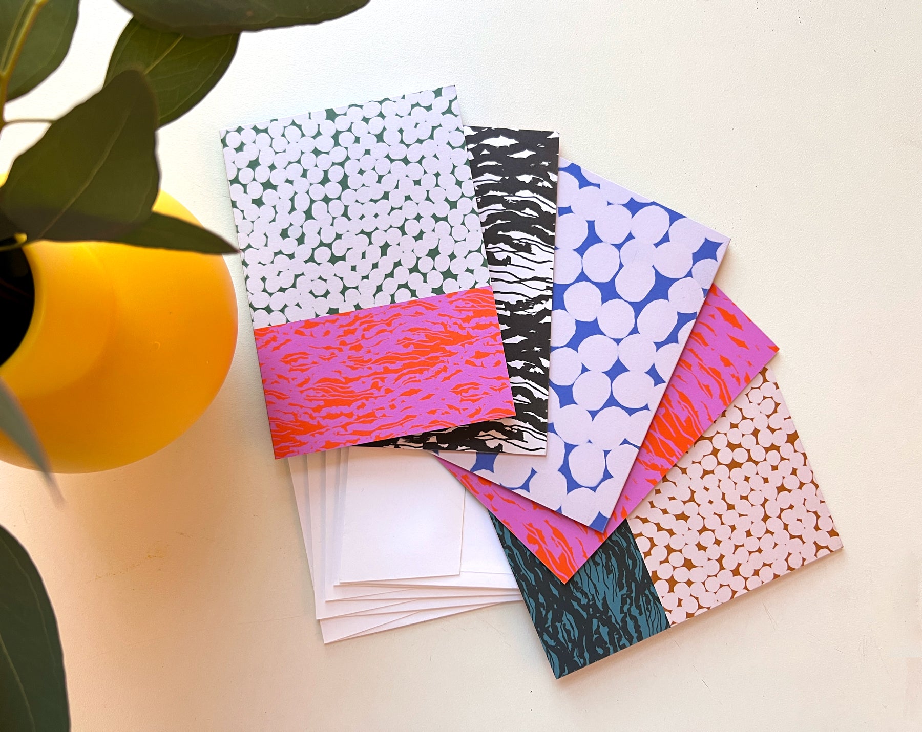 A pack of five folded note cards with various patterns, including dots and abstract designs, displayed alongside white envelopes on a neutral background. Designed by artist Leila Simon Hayes.