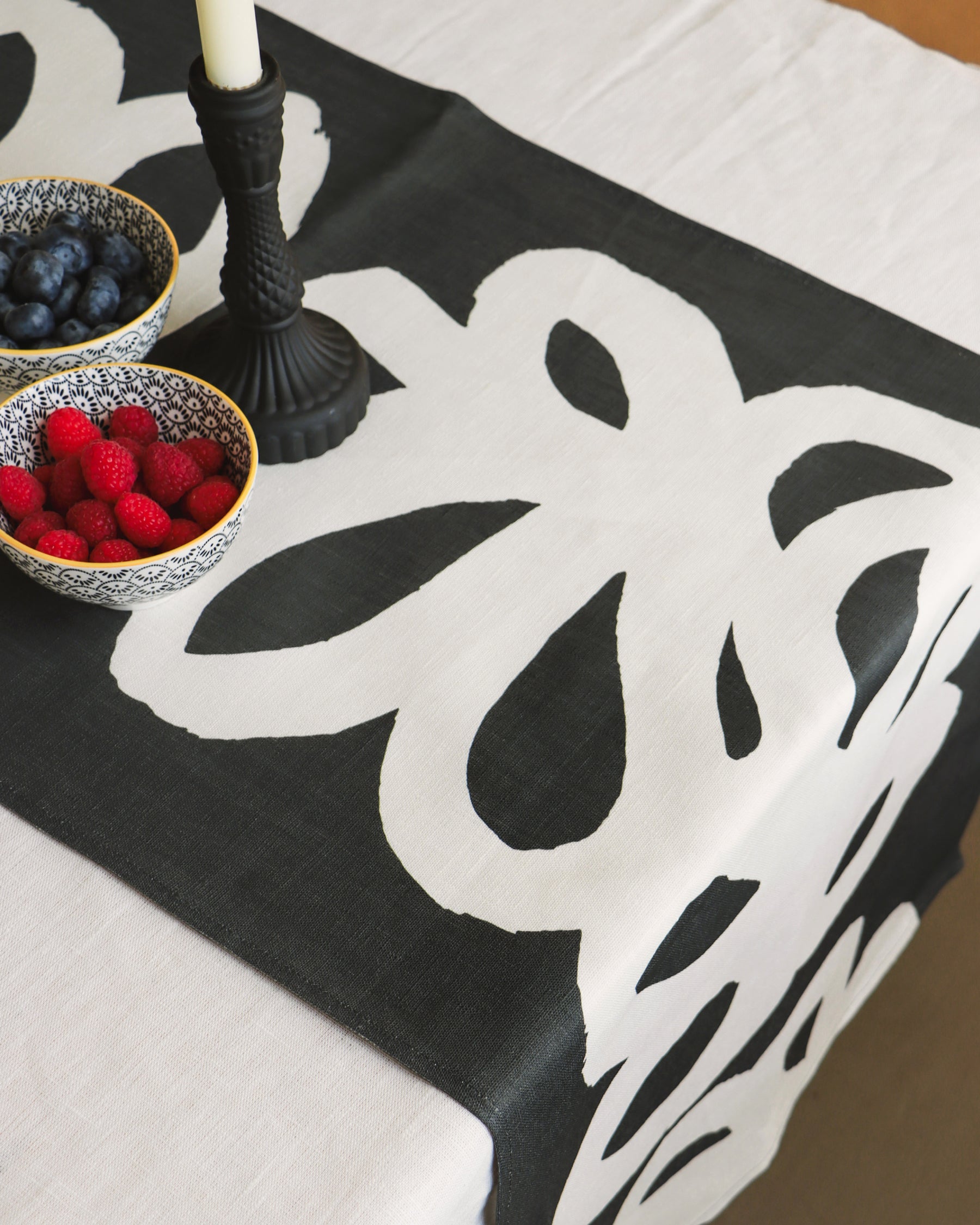 A black and white linen table runner with a floral pattern displayed on a table, part of a breakfast setting.