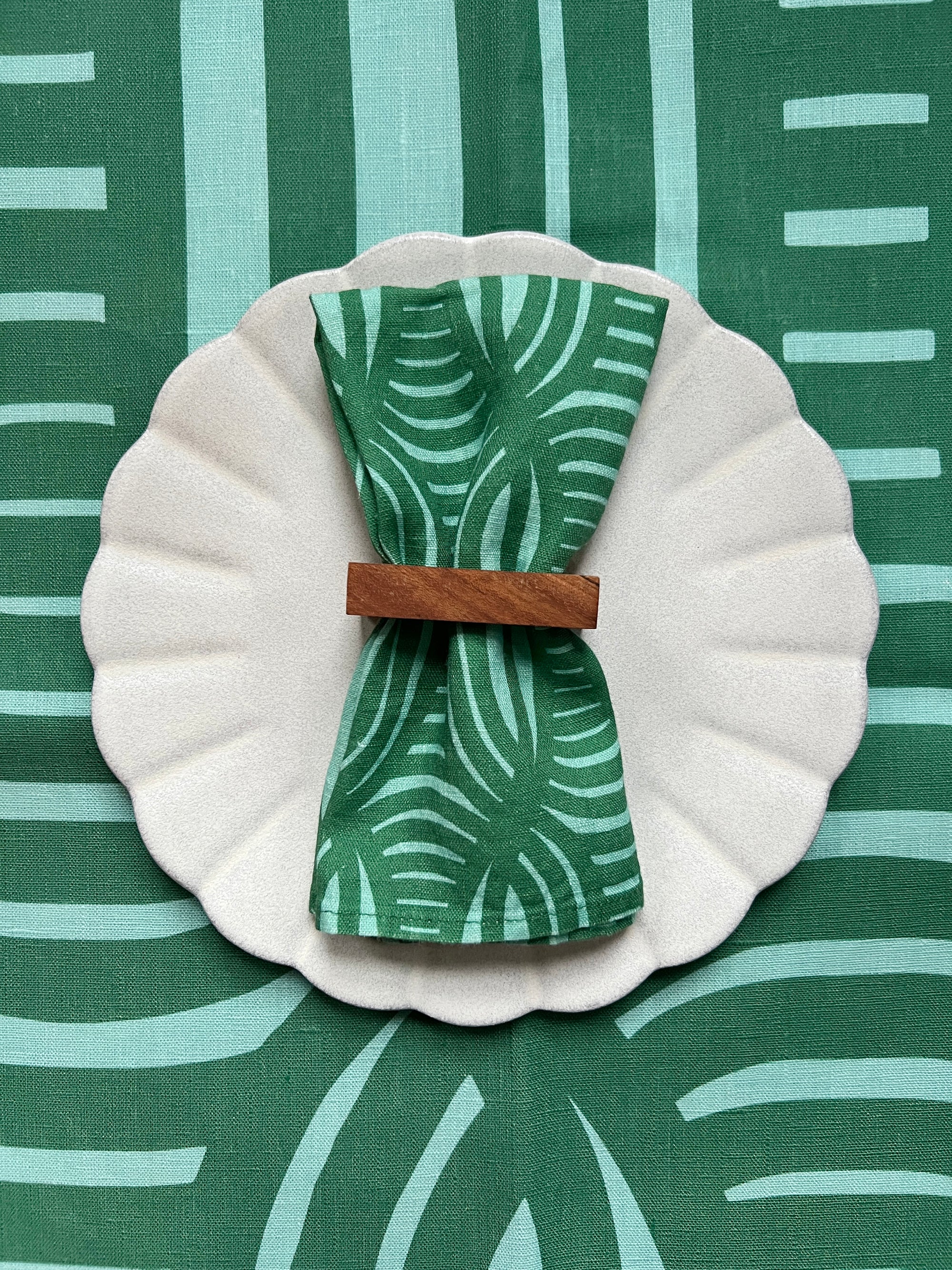 A green linen napkin with a striped geometric pattern, over a tablecloth with the same pattern. Designed by artist Leila Simon Hayes