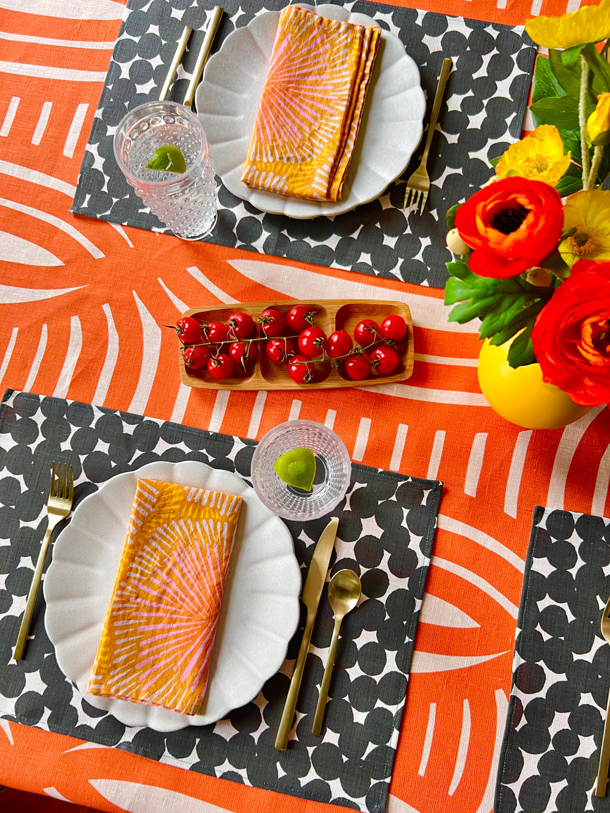 Creative dining table setting with bright colored, patterned orange linen napkins, black and white dots placemats and a orange geometric tablecloth. Designed by artist Leila Simon Hayes
