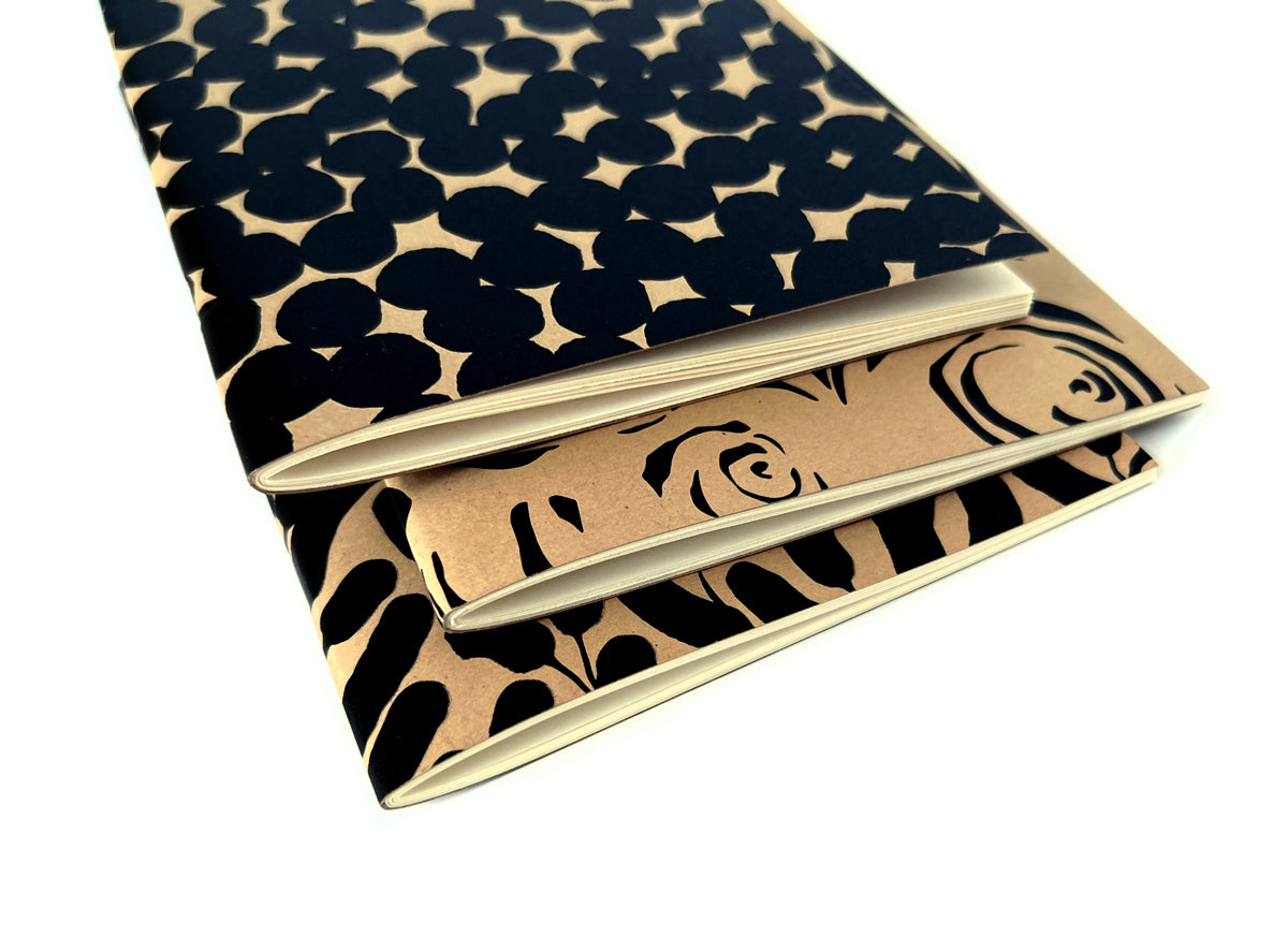 Three journals with black and beige patterns on a white background. Designed by artist Leila Simon Hayes.