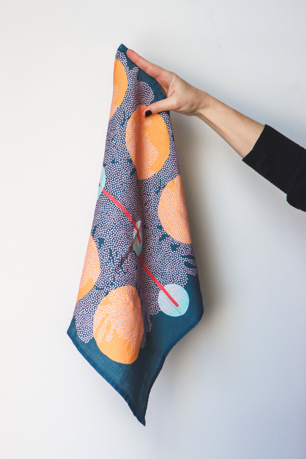 A hand holding out a blue napkin with organic colorful shapes. Designed by artist Leila Simon Hayes. 