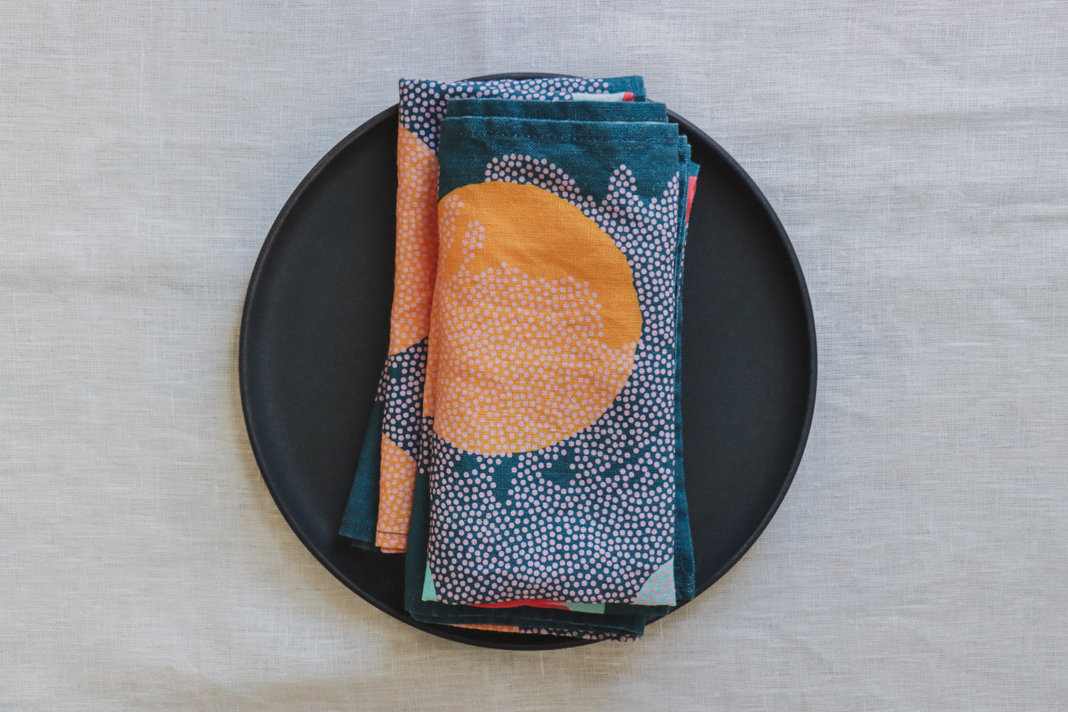 A navy blue linen napkin with an abstract pattern is displayed on a black plate, with a neutral background. Designed by artist Leila Simon Hayes. 