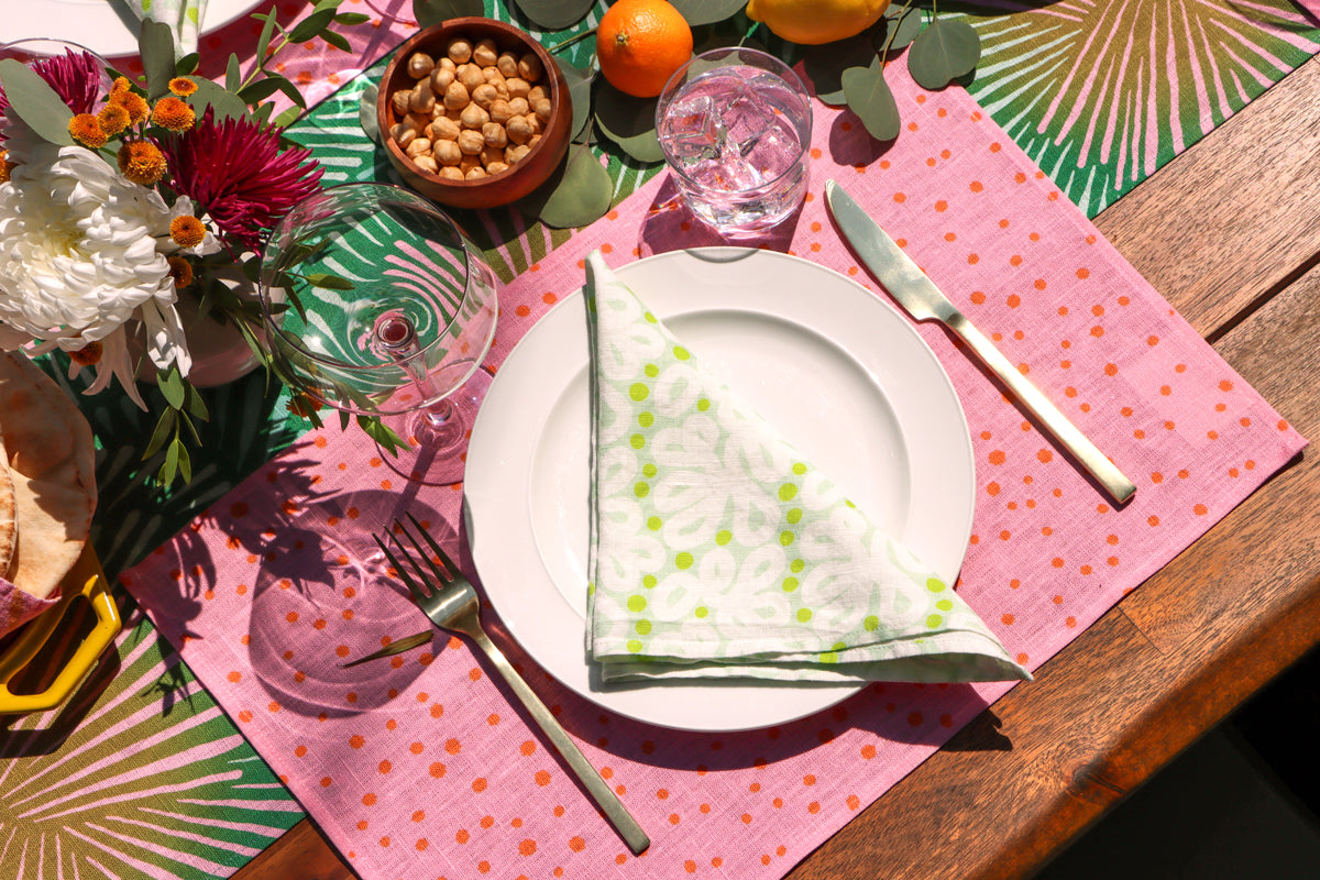 Table setting with a green napkin, pink polka dot placemat, and green sunburst table runner all designed by artist Leila Simon Hayes.