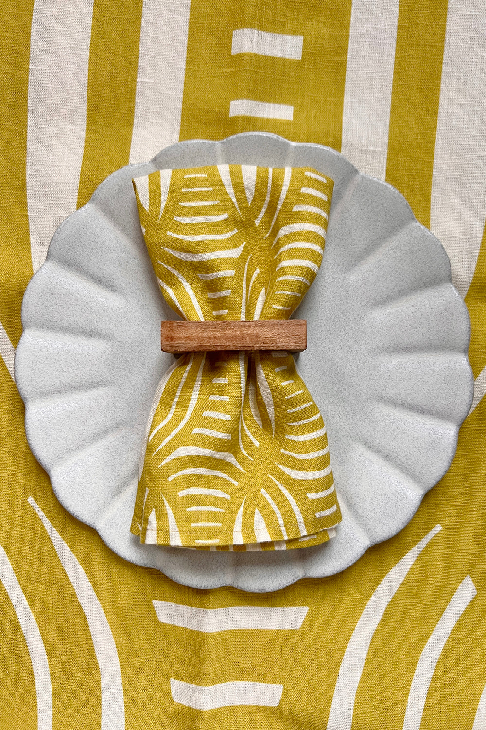 Yellow and white linen dinner napkins with unique stripe pattern over a yellow tablecloth with the same pattern. Designed by artist Leila Simon Hayes