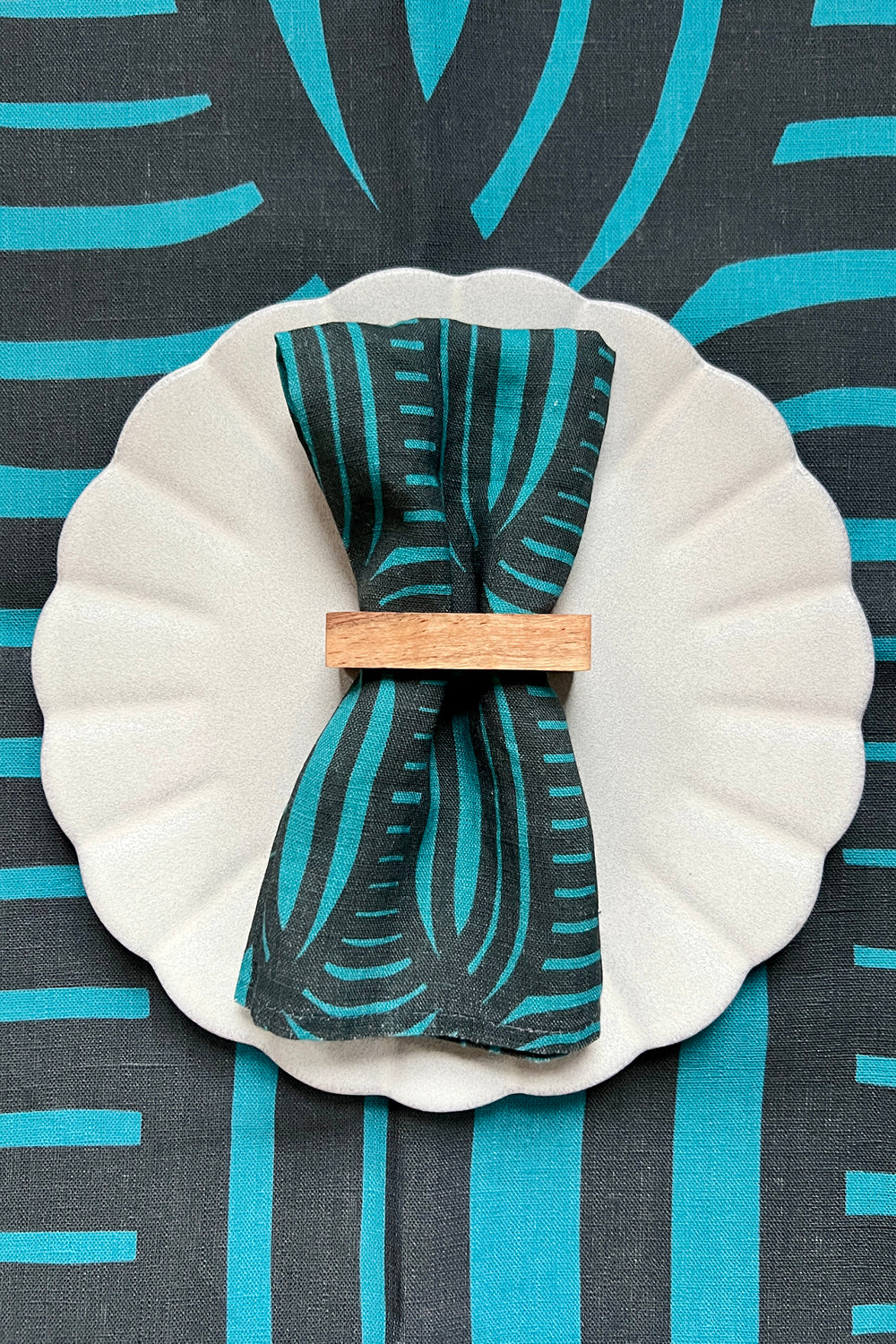 A blue linen napkin with a geometric pattern is displayed on a white plate, over a tablecloth with the same pattern and color. designed by artist Leila Simon Hayes