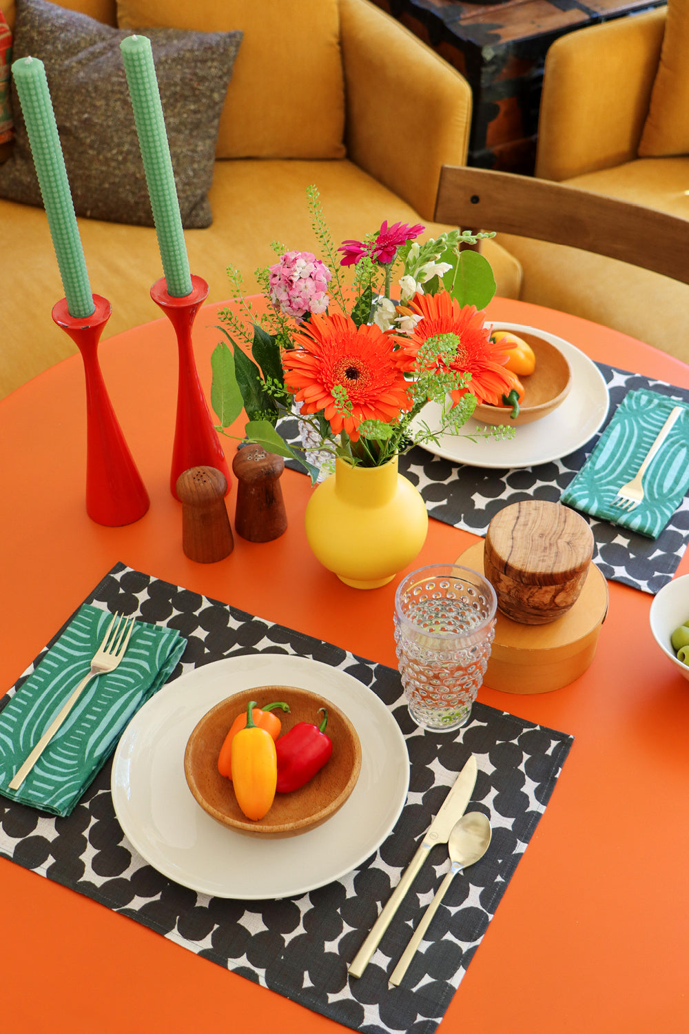Colorful table setting with green striped napkins, black and white dots, on an orange table. Designed by artist Leila Simon Hayes