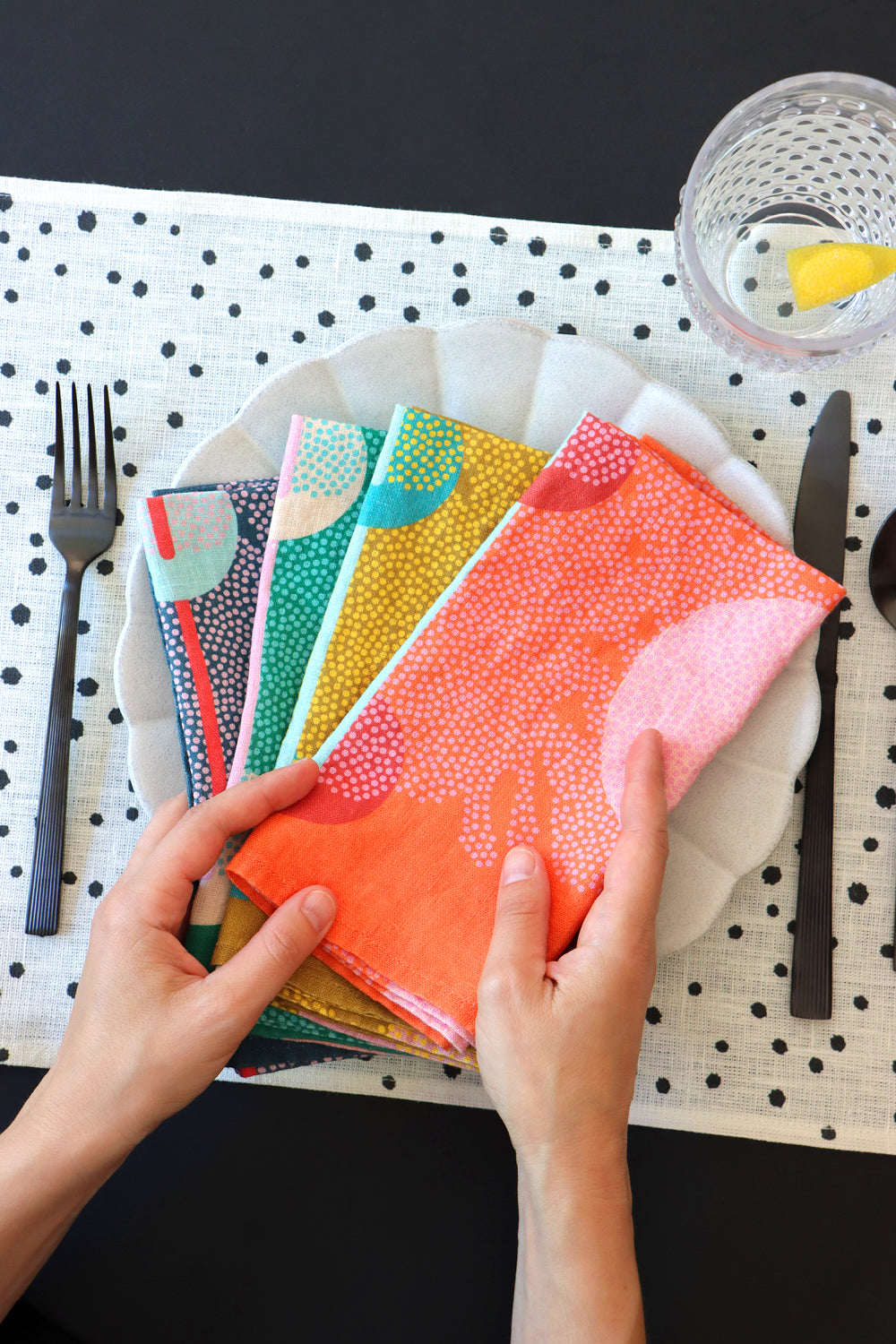 Four colorful patterned napkins on a plate over a black and white polka dot placemat. Designed by artist Leila Simon Hayes.