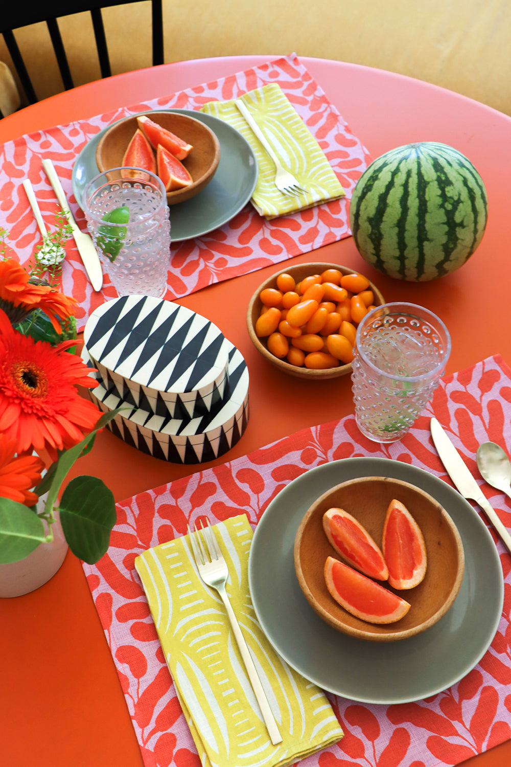 Colorful table setting with plates, yellow striped napkins, pink and coral floral placemats and decorative fruits. Designed by artist Leila Simon Hayes