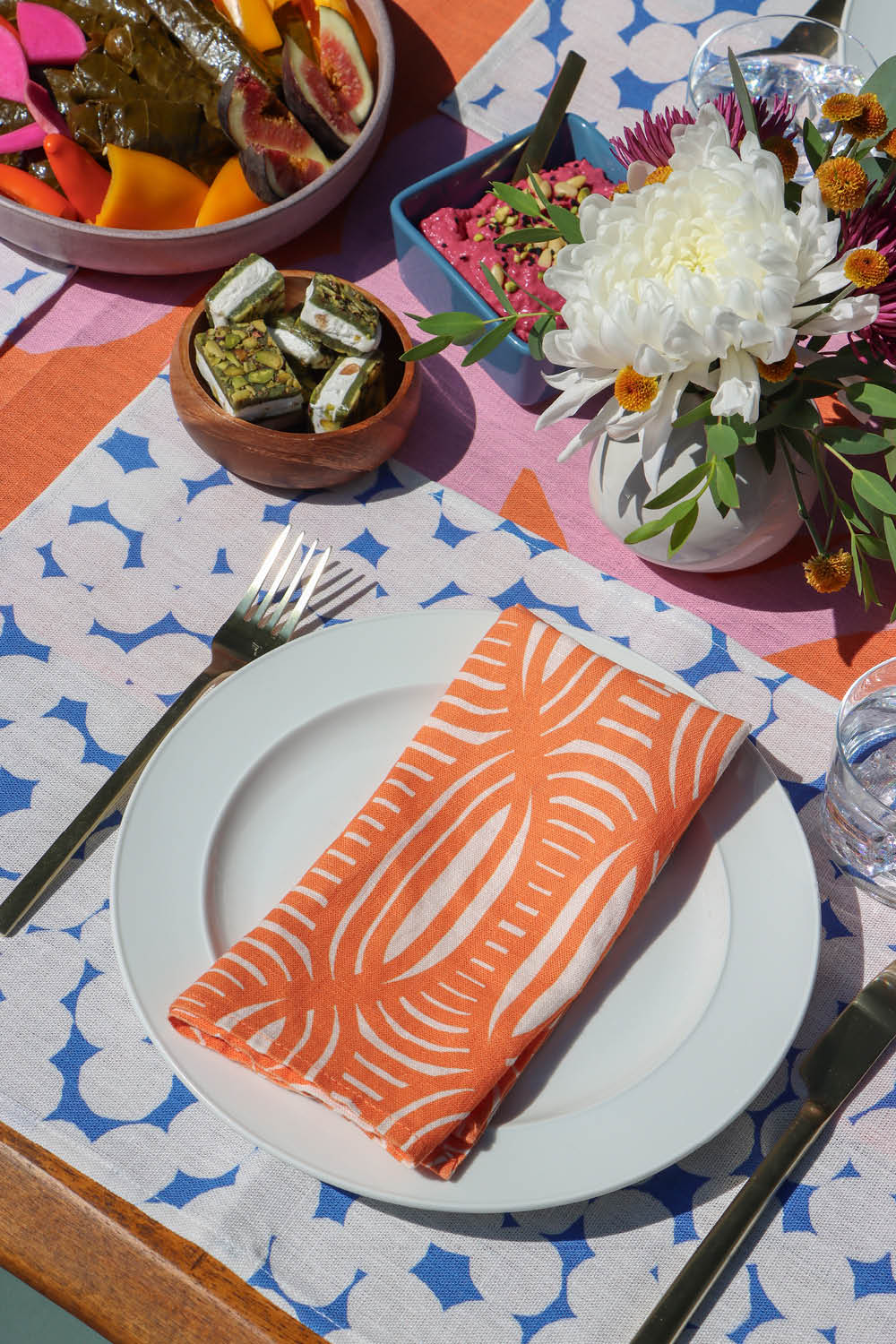 Dining table setting with a coral striped dinner napkin, blue and white dotted placemat, and a pink and coral table runner. Designed by artist Leila Simon Hayes