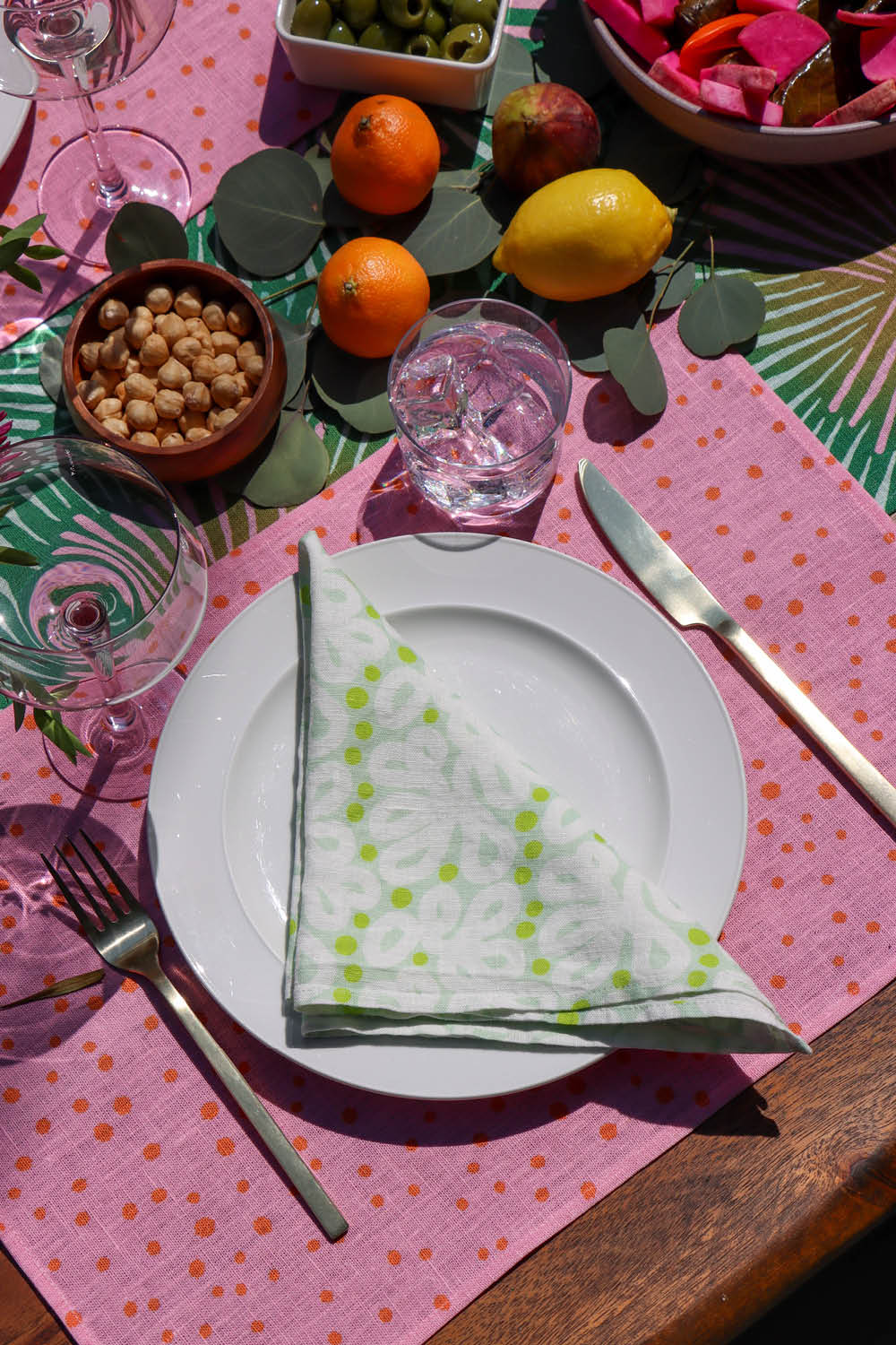 Table setting with a pink polka dot placemat, green napkin, and green table runner. Designed by artist Leila Simon Hayes