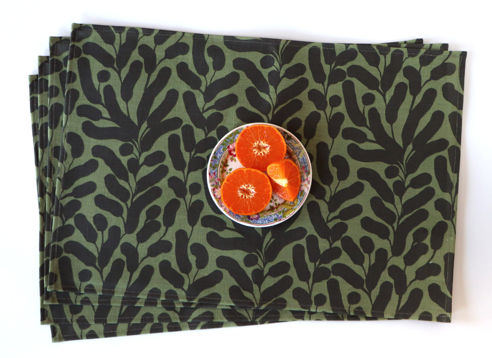 Four stacked olive green placemat with black botanical leaf pattern on a white background. Designed by artist Leila Simon Hayes