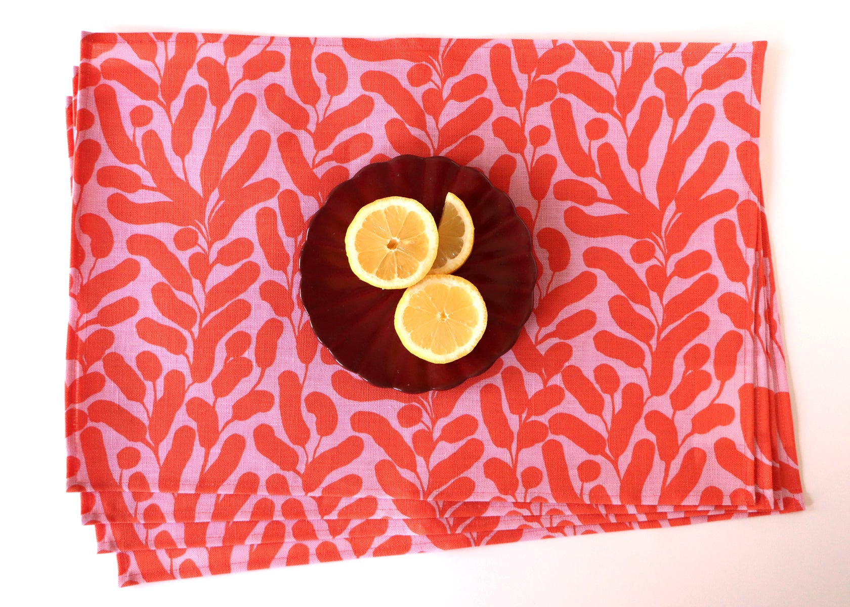 Four layered placemats with a pink background and coral botanical leaf design. Designed by artist Leila Simon Hayes