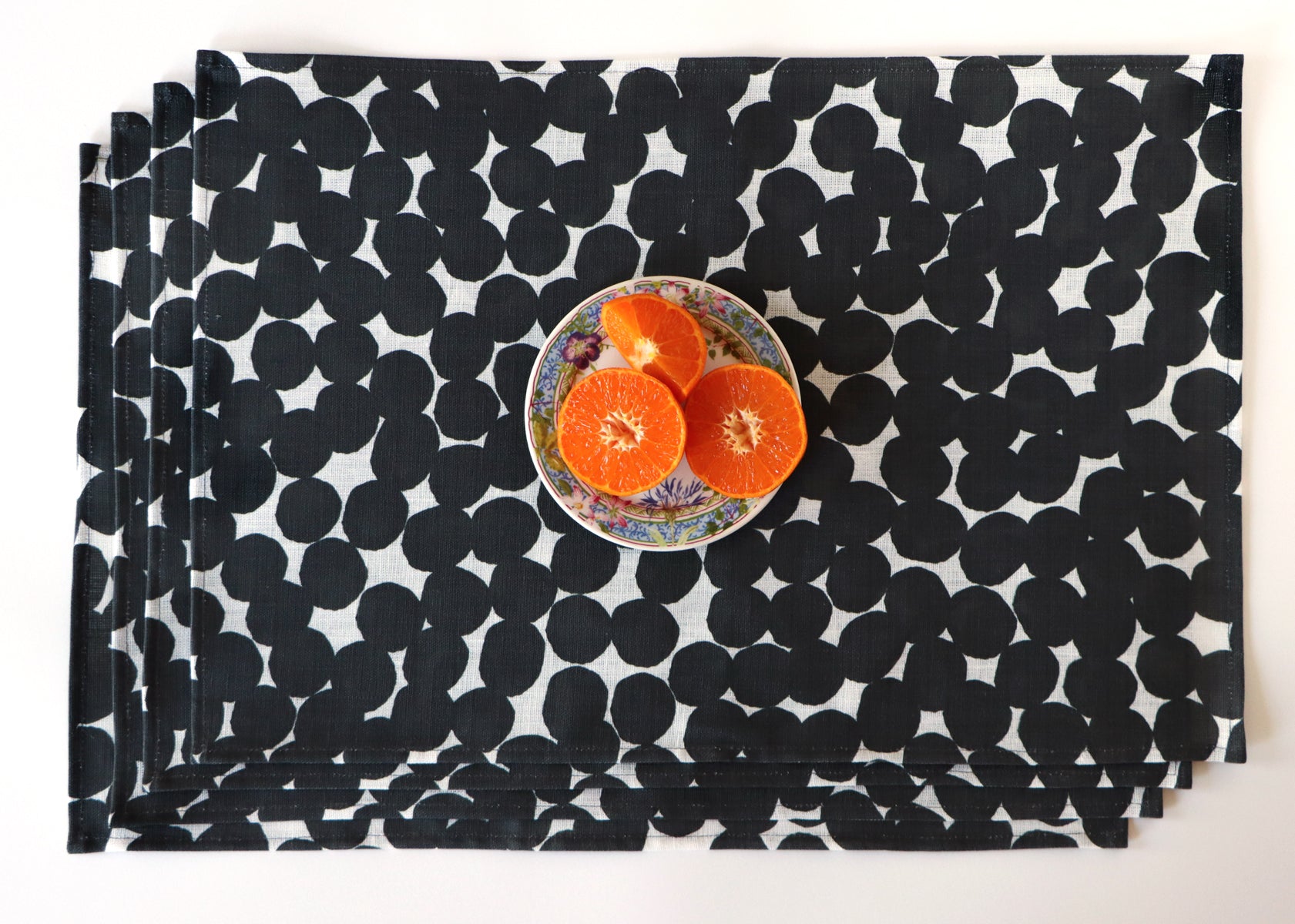 Set of four black and white dot patterned placemats with a plate of oranges on a matching tablecloth. Designed by artist Leila Simon Hayes