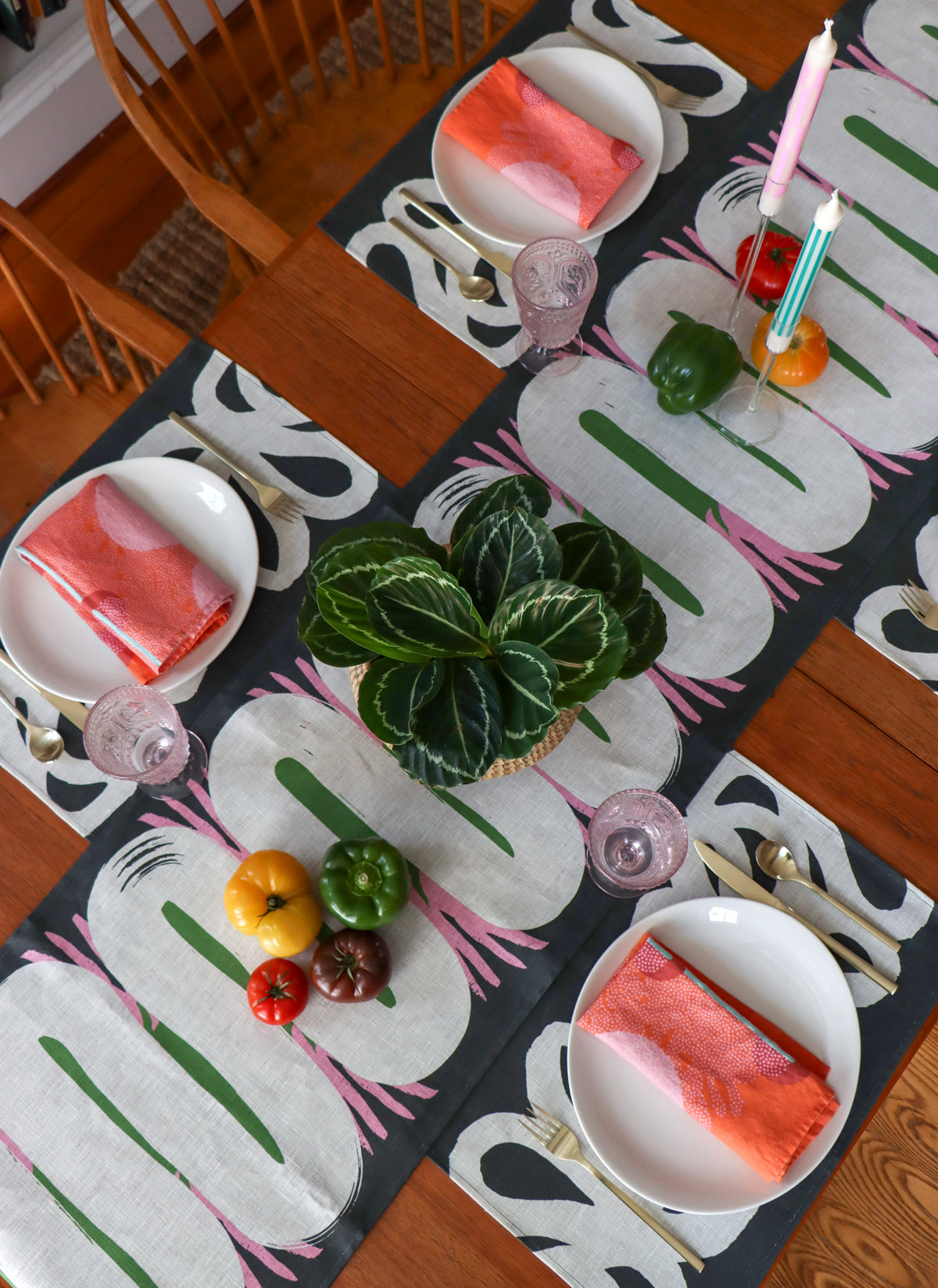 A dining room table set for dinner with coral napkins, black and white abstract placemats and a table runner with organic shapes. Designed by artist Leila Simon Hayes.