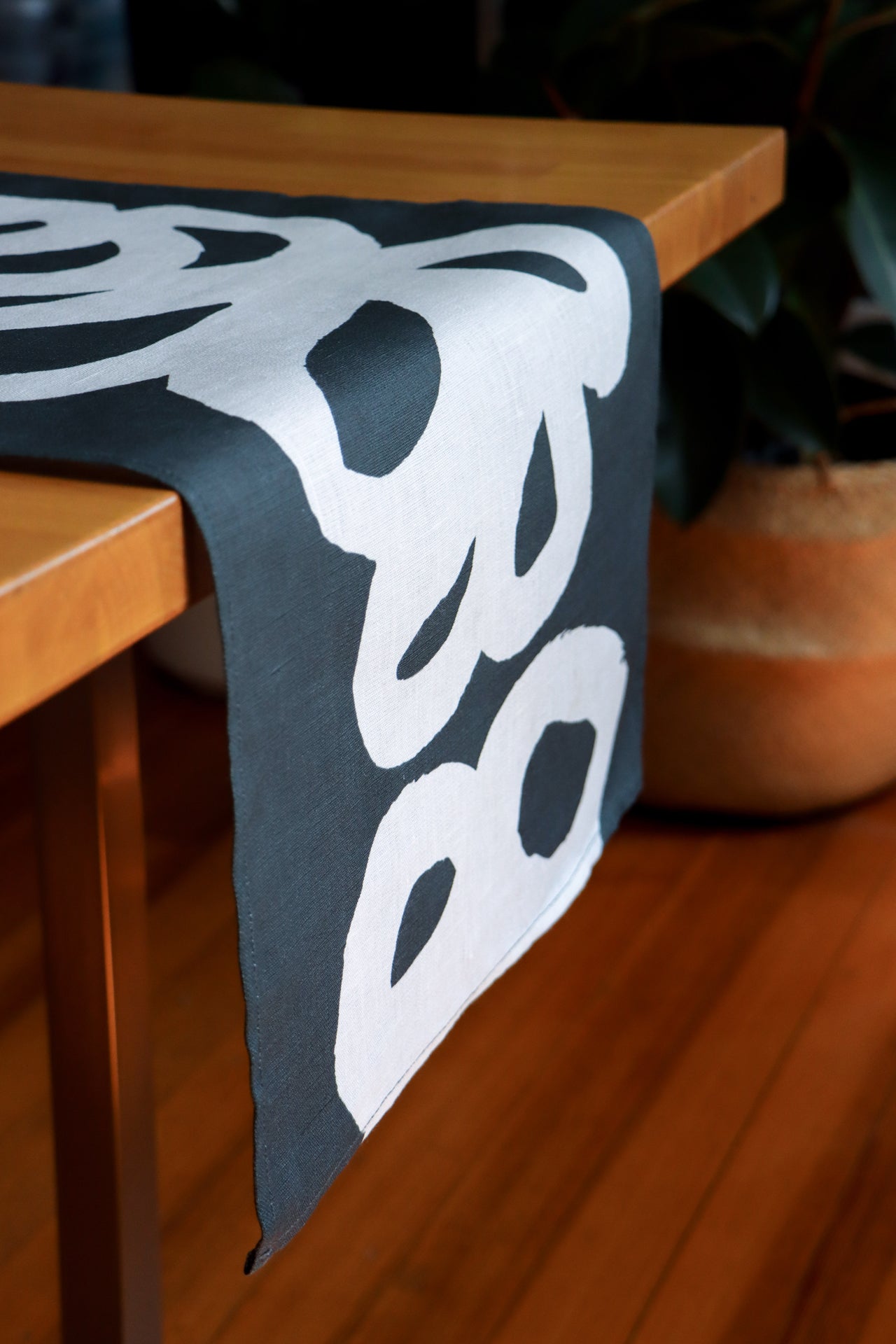 Black table runner with white floral lace design on a wooden table. Designed by artist Leila Simon Hayes.