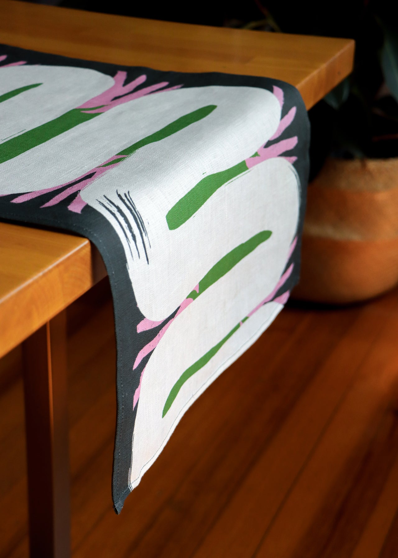 Decorative table runner with leaf pattern and organic shapes on a wooden table. Designed by artist Leila Simon Hayes.