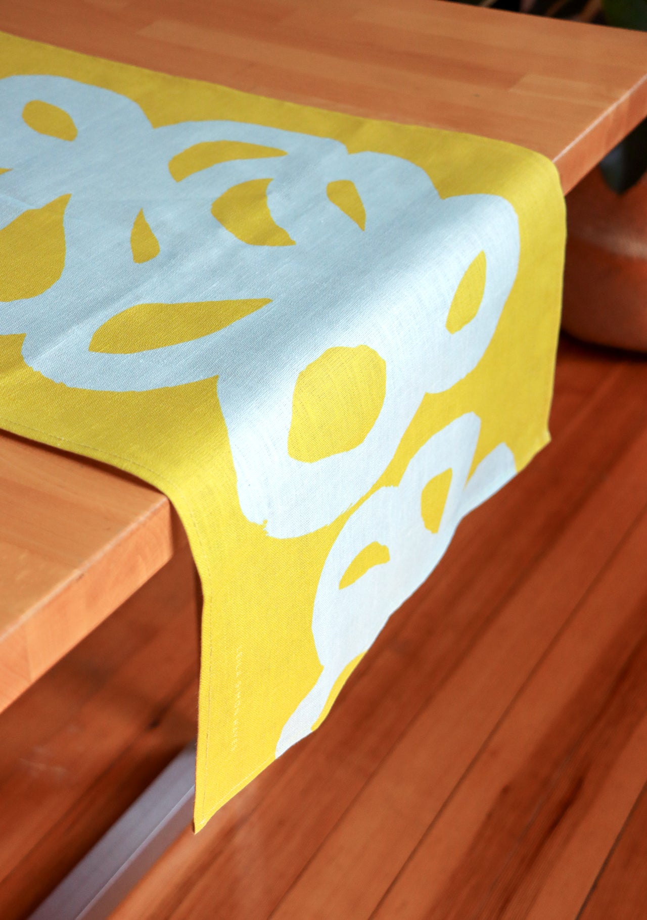 Green table runner with light blue floral lace design, draped over a wooden table. Designed by artist Leila Simon Hayes.