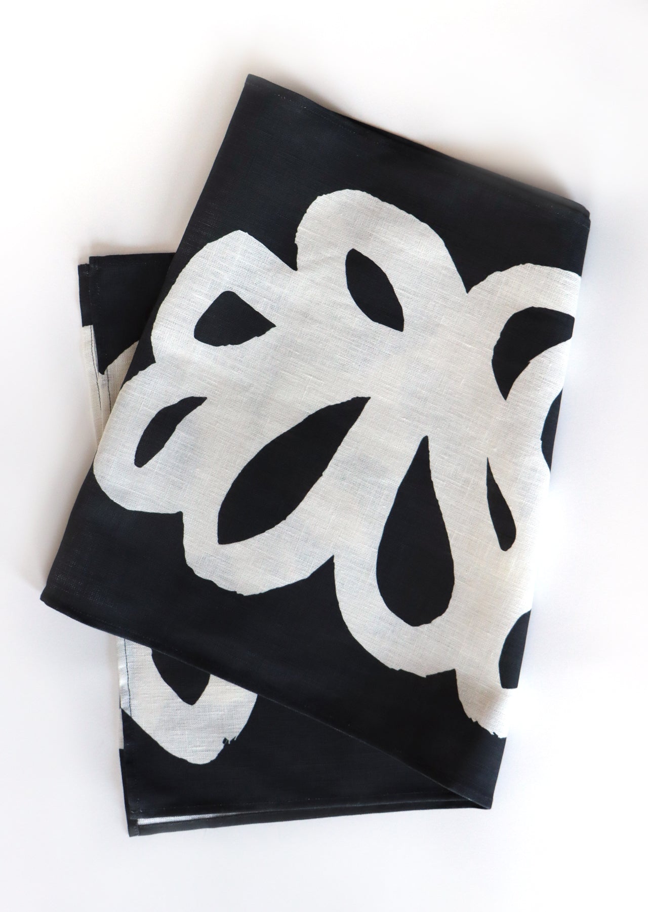 Black table runner with white floral loops pattern, designed by artist Leila Simon Hayes. Table runner is folded on a white background.
