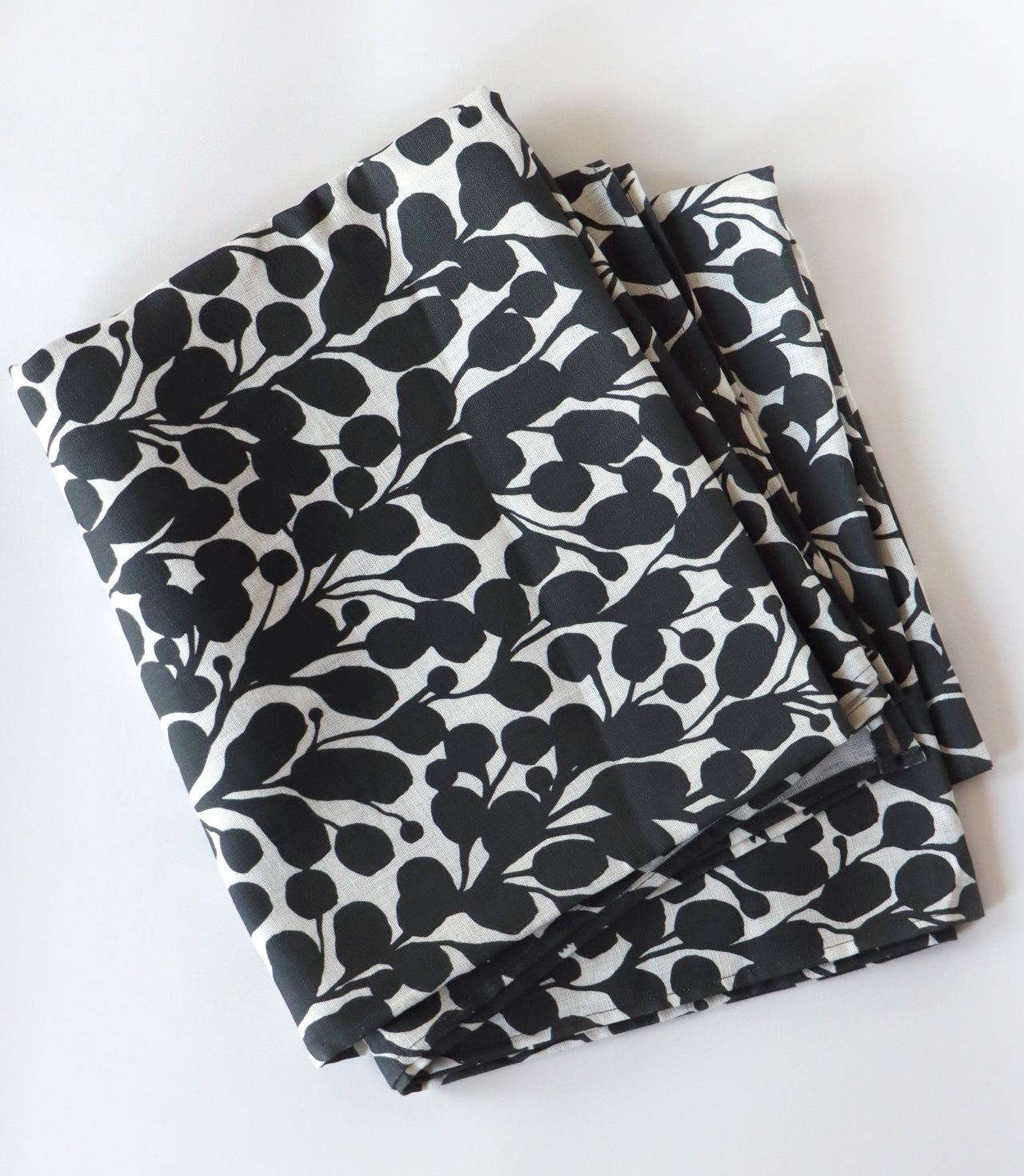 Folded black and white floral tablecloth on a white background. Designed by artist Leila Simon Hayes.