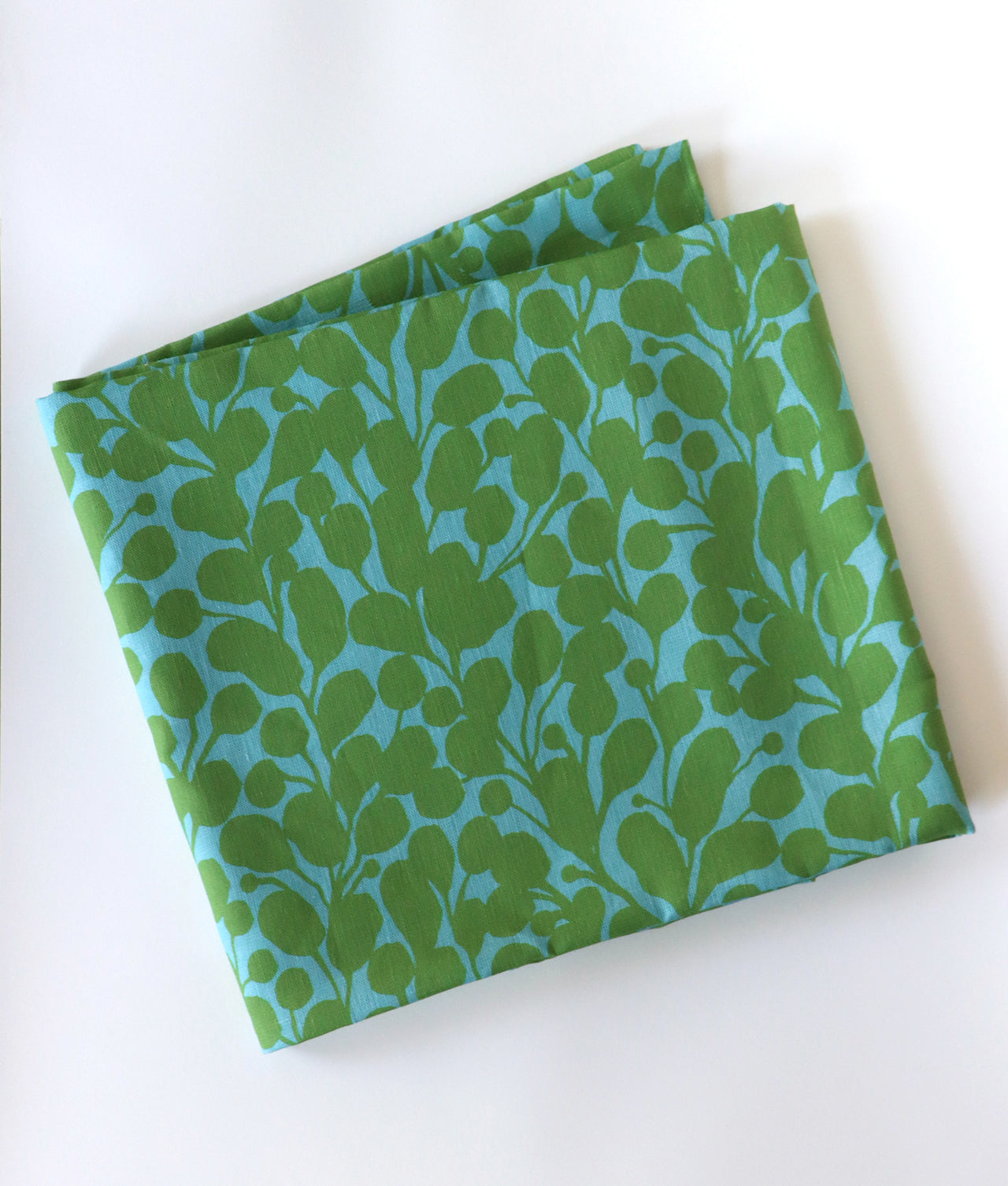 Blue and green botanical tablecloth folded over a white background. Designed by artist Leila Simon Hayes.