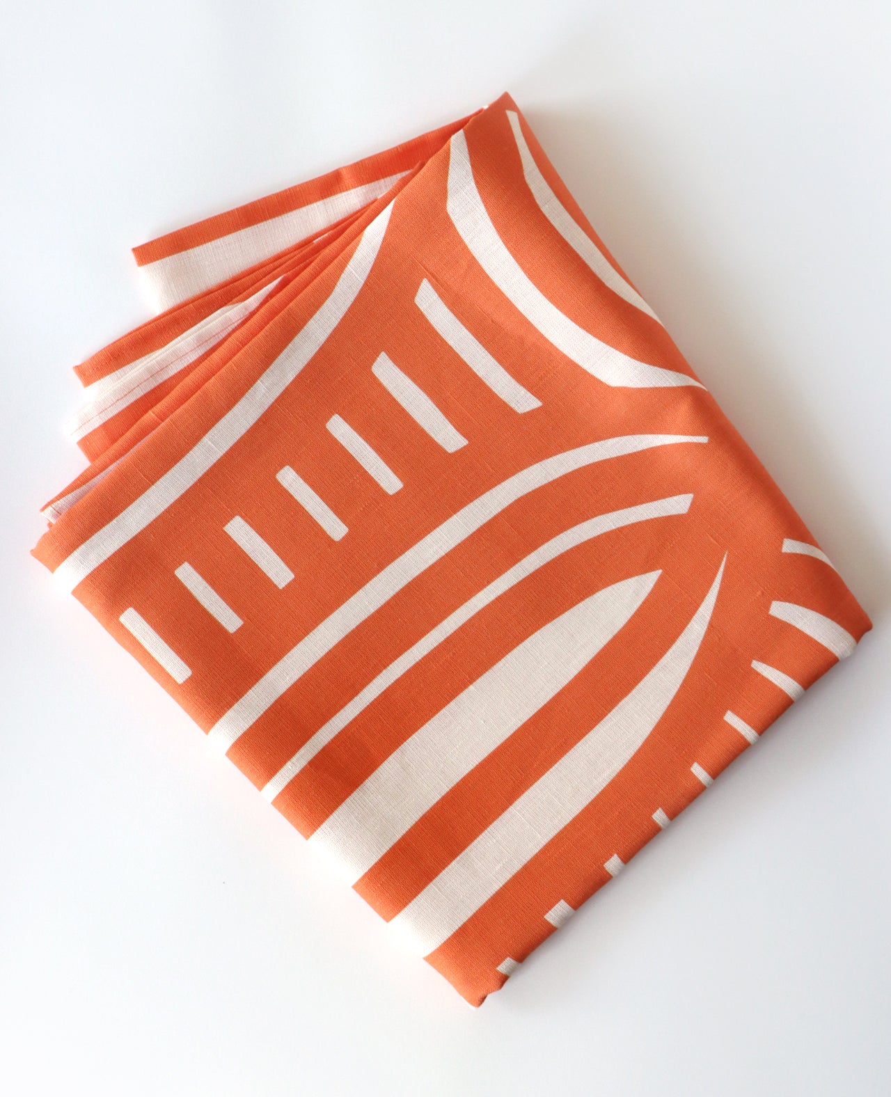A folded coral tablecloth against a white background. Designed by artist Leila Simon Hayes.