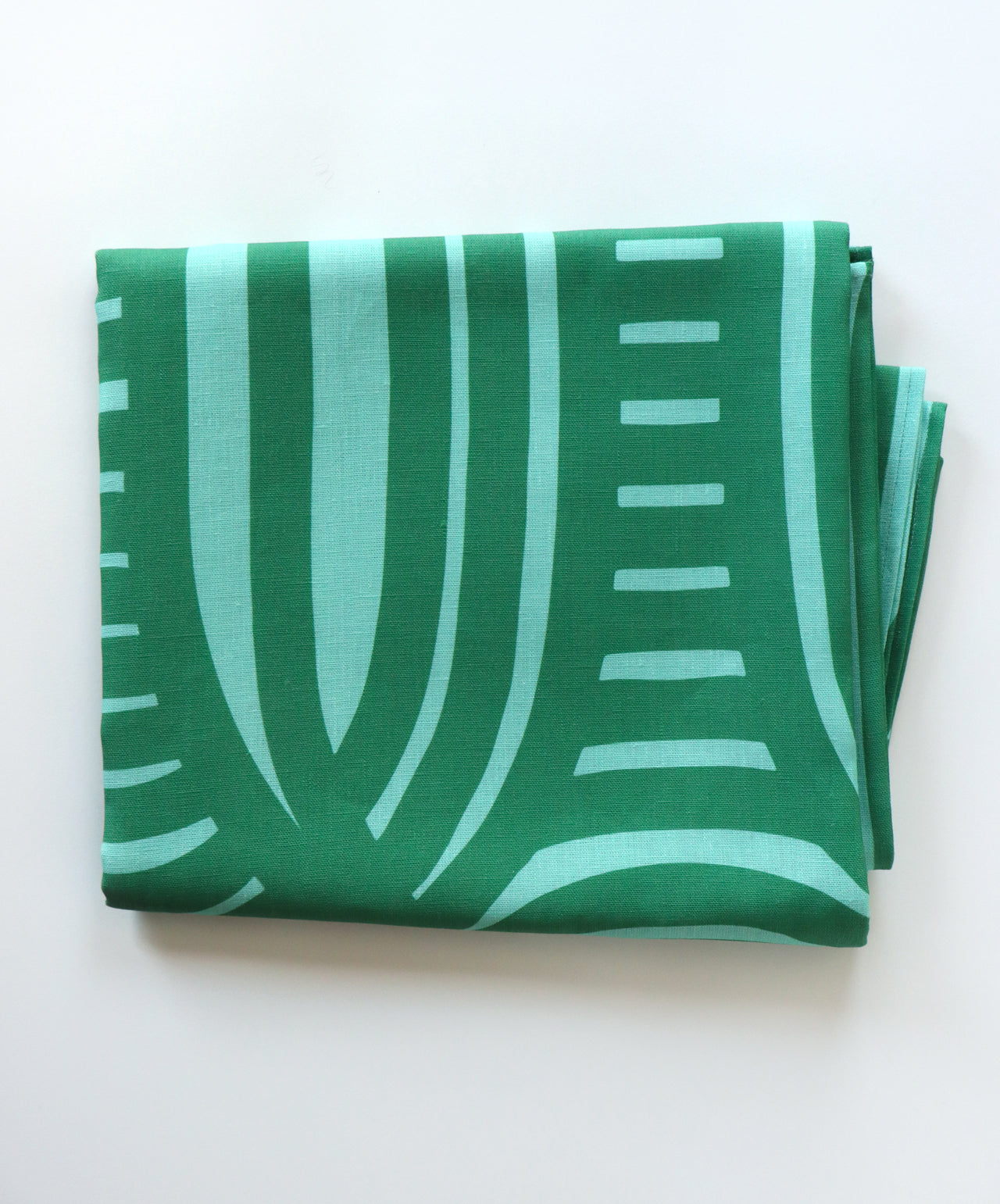 Folded green tablecloth with a stripe pattern on a white background. Designed by artist Leila Simon Hayes.