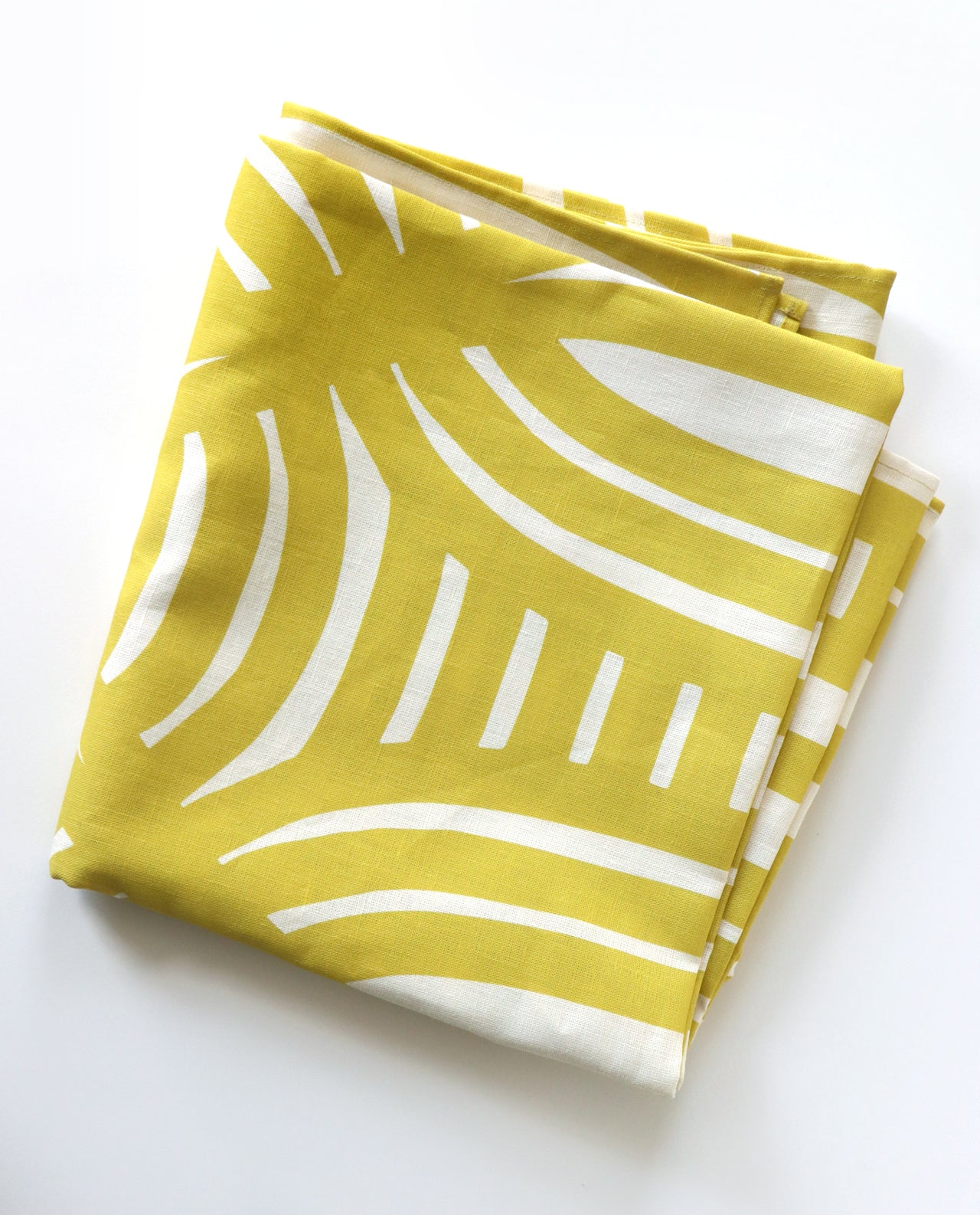 Yellow folded tablecloth with geometric stripe pattern on a white background. Designed by artist Leila Simon Hayes.