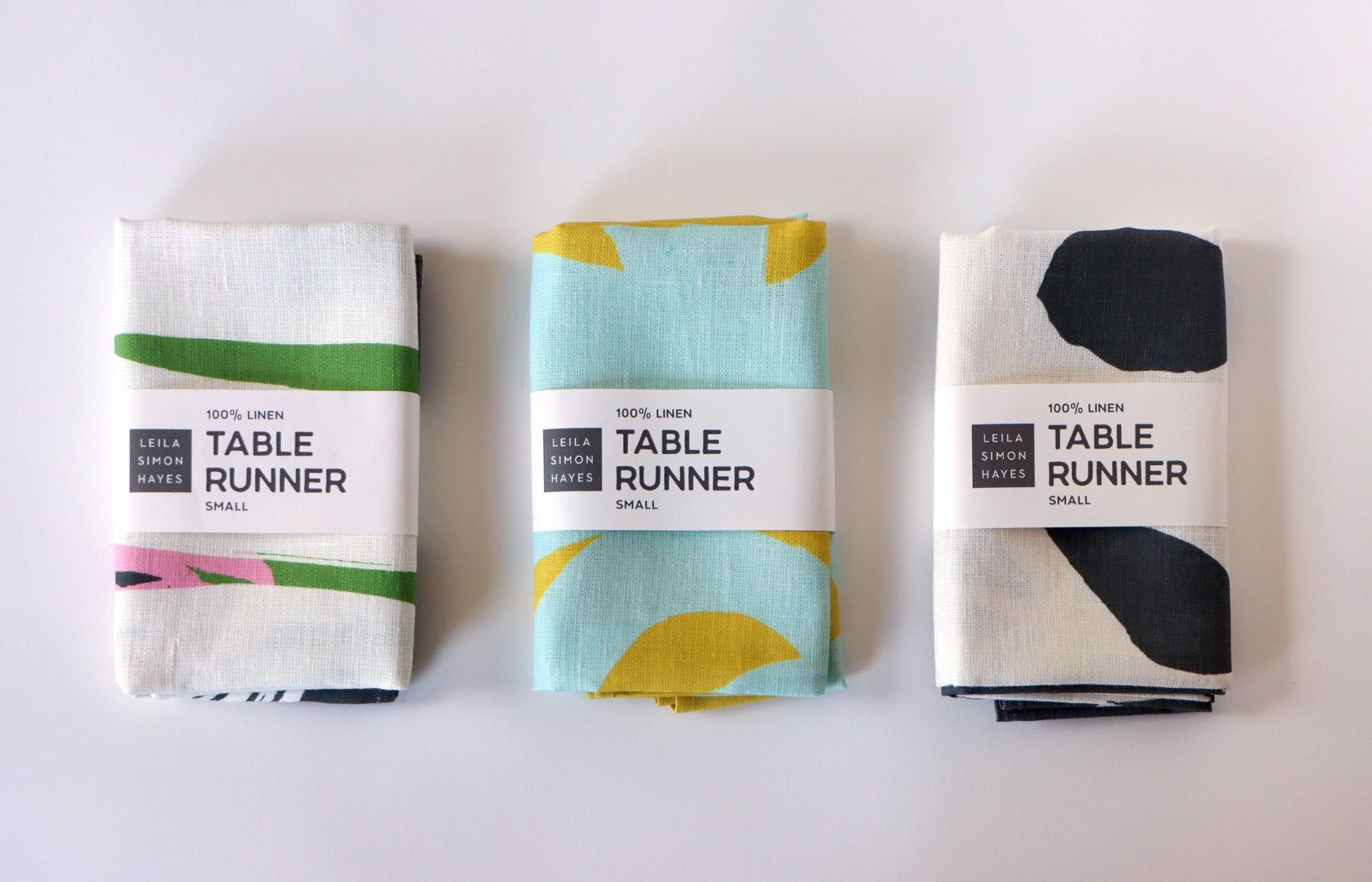 Three table runner packages with different designs on a white background, designed by artist Leila Simon Hayes.