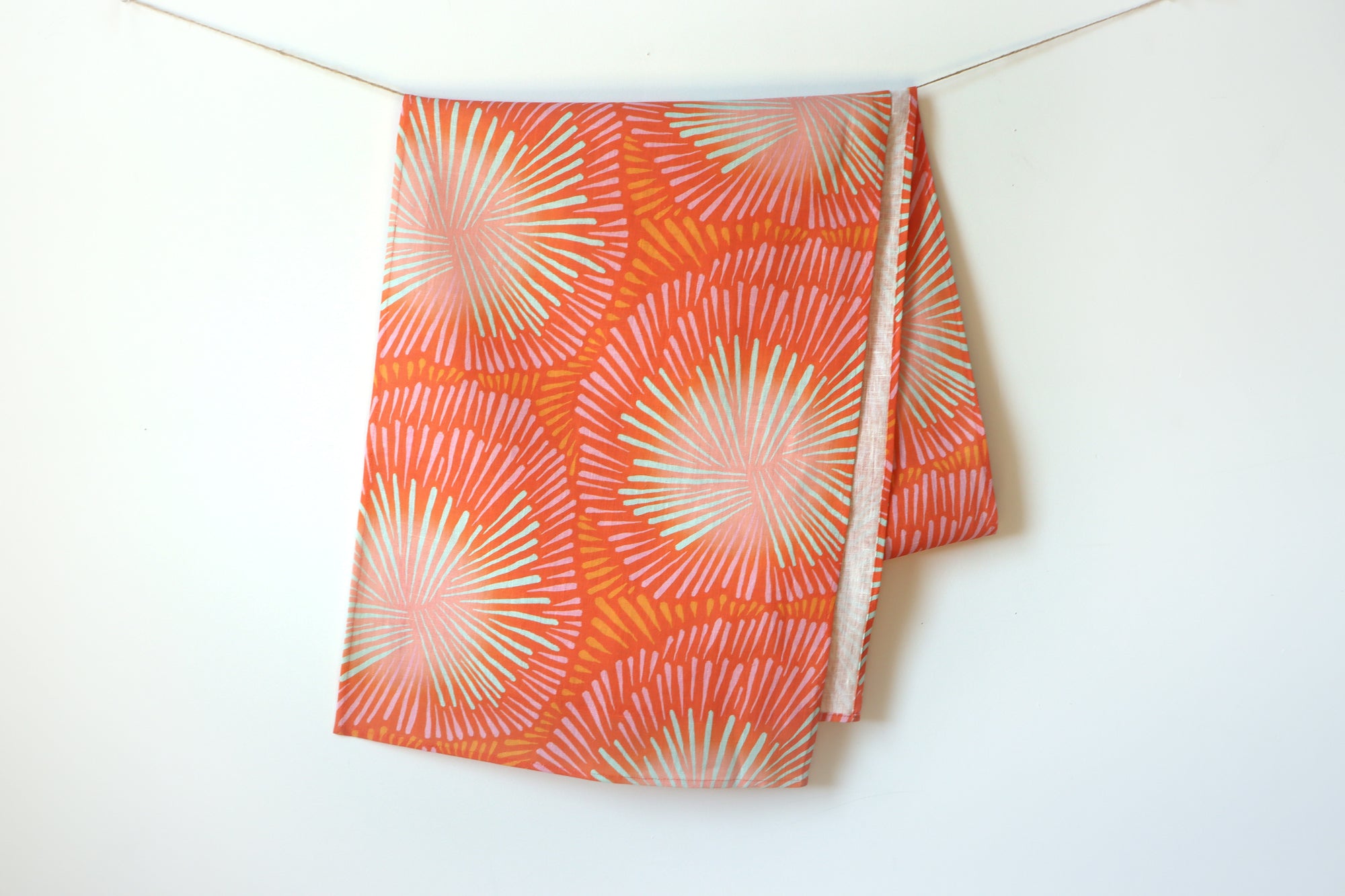 A red burst table runner hanging on a white background, designed by artist Leila Simon Hayes.