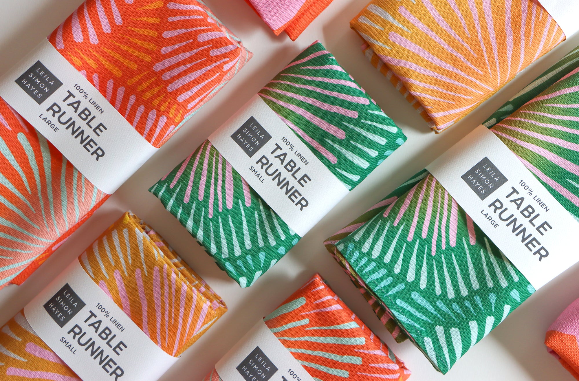 Colorful table runner packages with burst patterns and brand labels saying "100% Linen Table Runner", designed by artist Leila Simon Hayes.