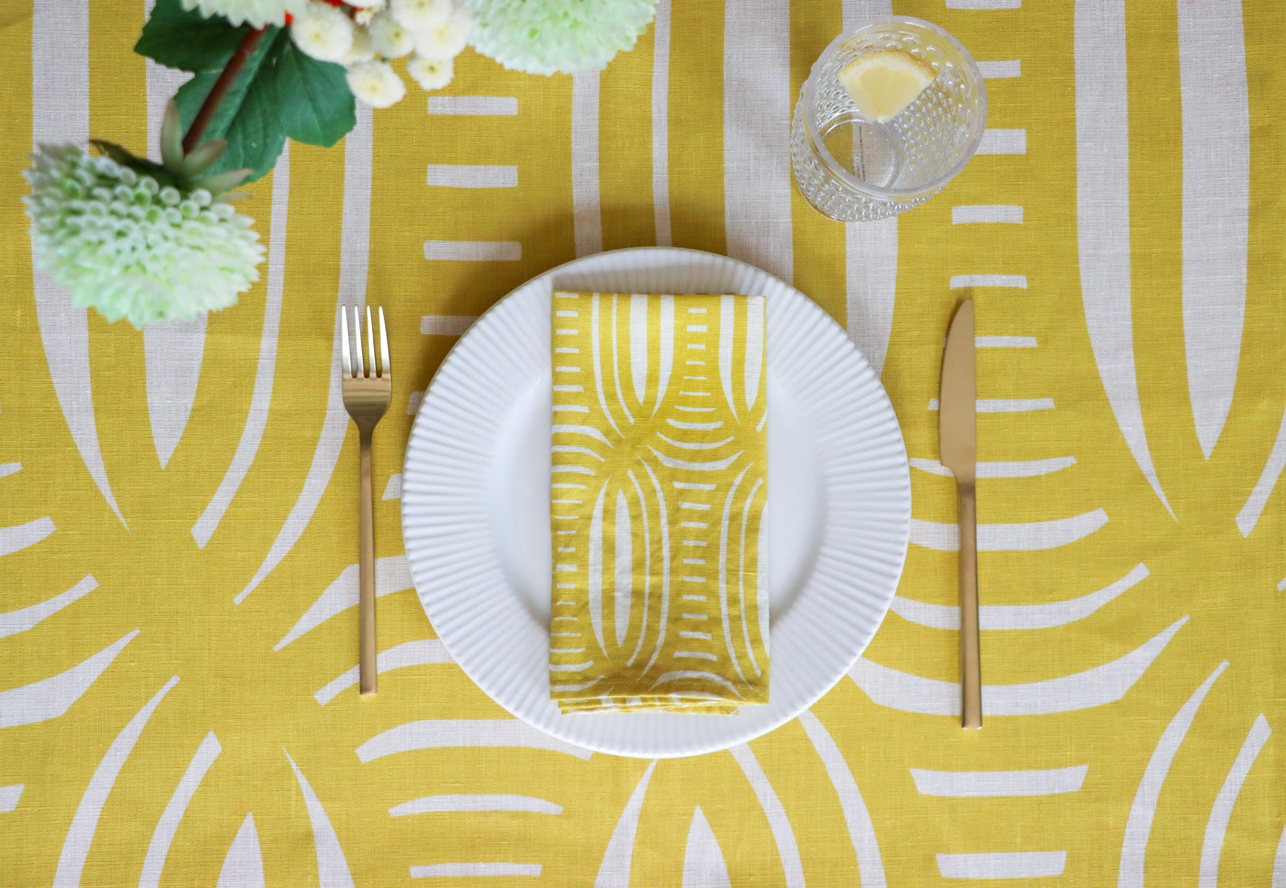 Yellow stripe patterned tablecloth with a plate and yellow napkin, designed by artist Leila Simon Hayes.