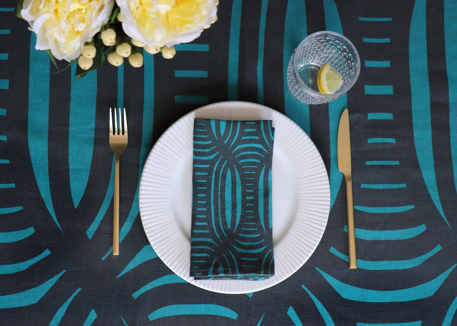 Table setting with a navy blue and blue patterned tablecloth, white plate, gold fork and knife. Designed by artist Leila Simon Hayes.