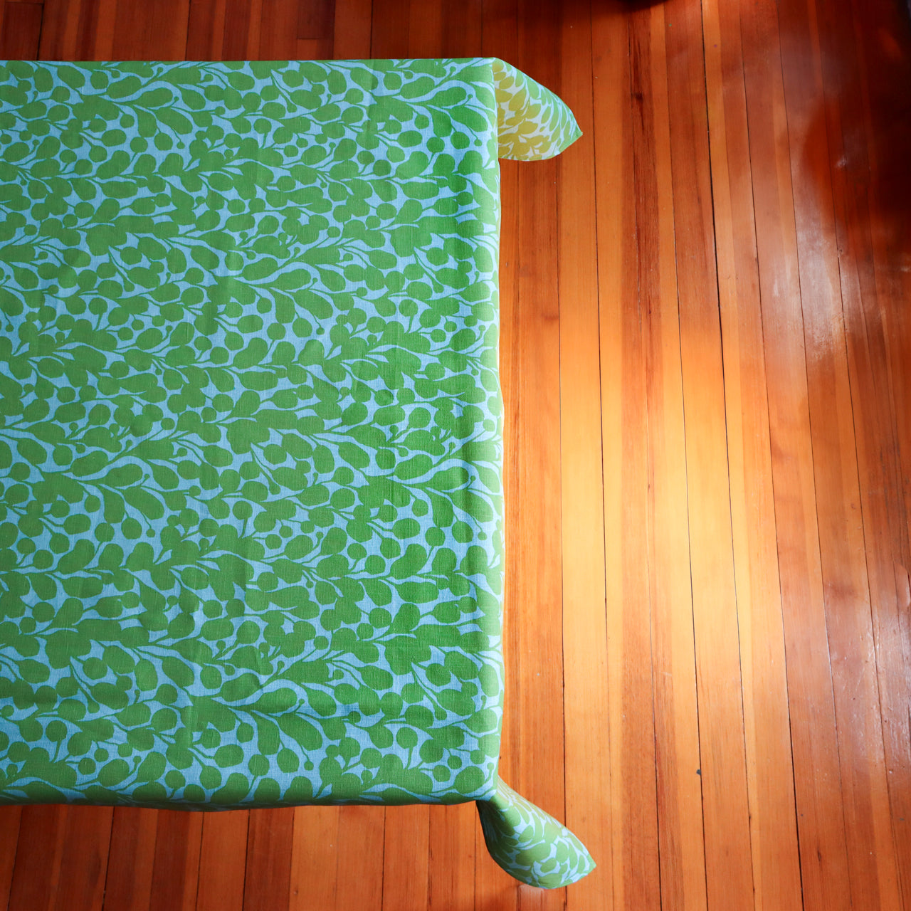 Green and blue floral patterned fabric on a table with a wooden floor background. Designed by artist Leila Simon Hayes.