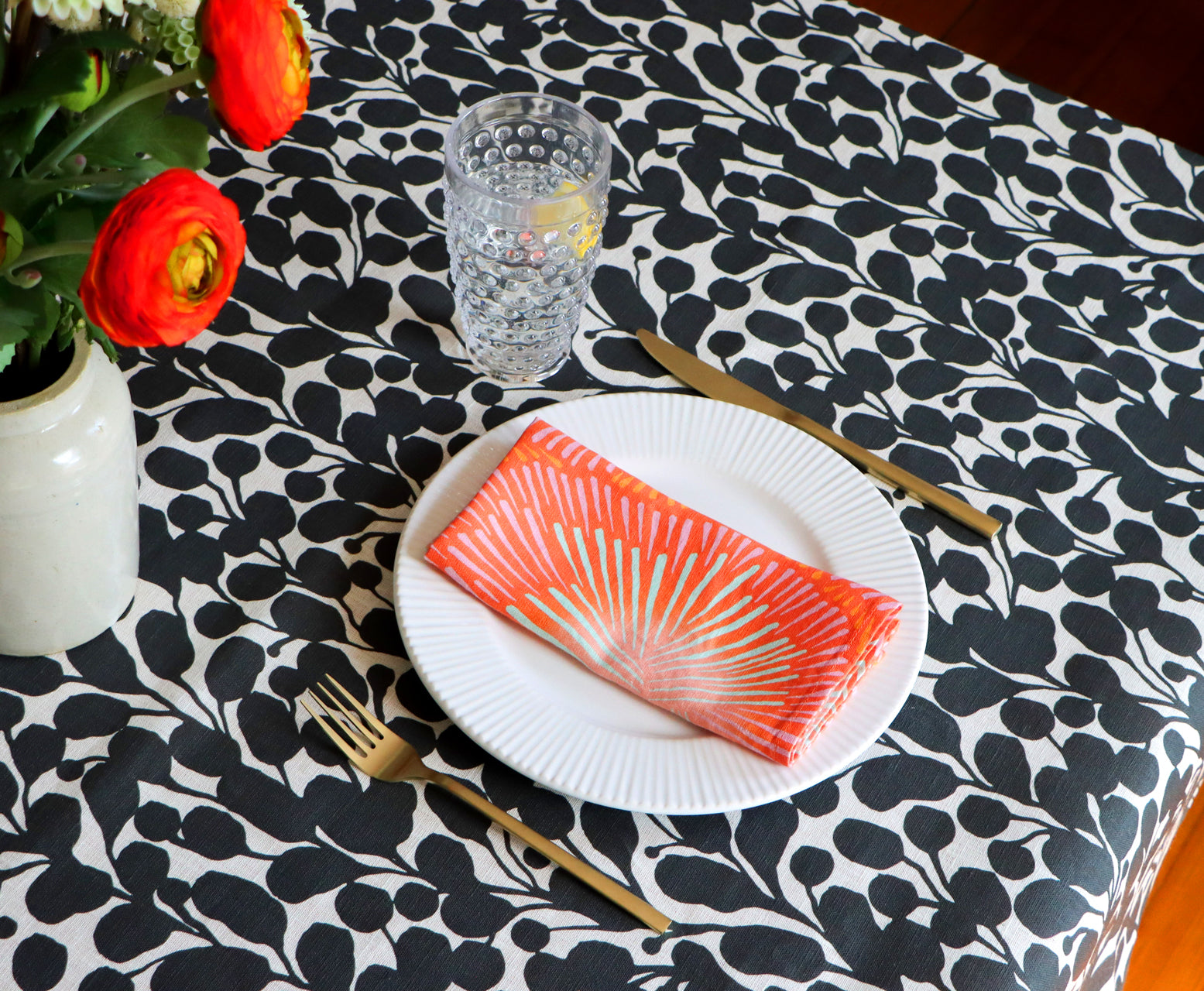Coral burst napkin on a white plate over a black and white botanical patterned tablecloth. Designed by artist Leila Simon Hayes.
