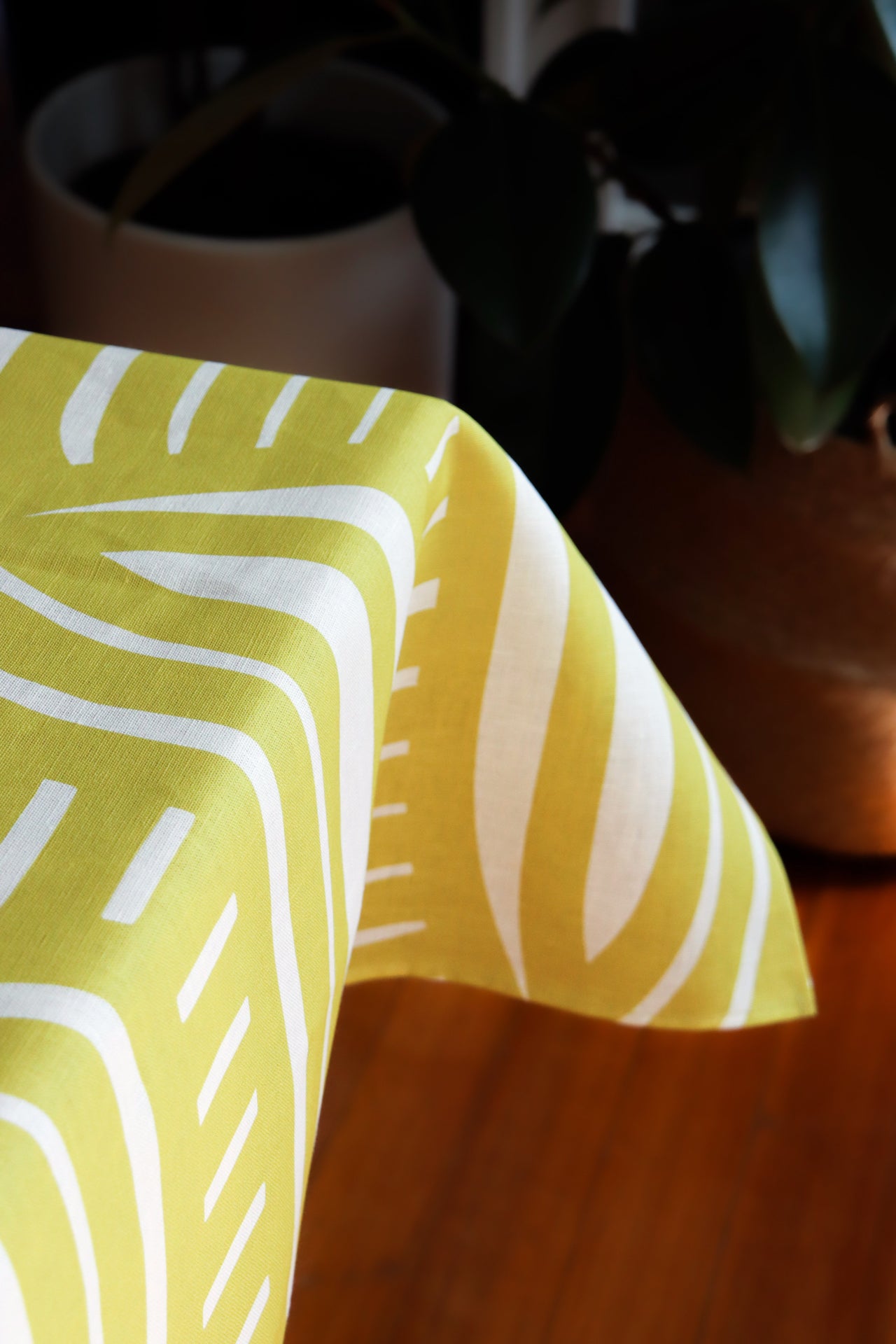Yellow tablecloth with light yellow geometric pattern on a table with a blurred background. Designed by artist Leila Simon Hayes.