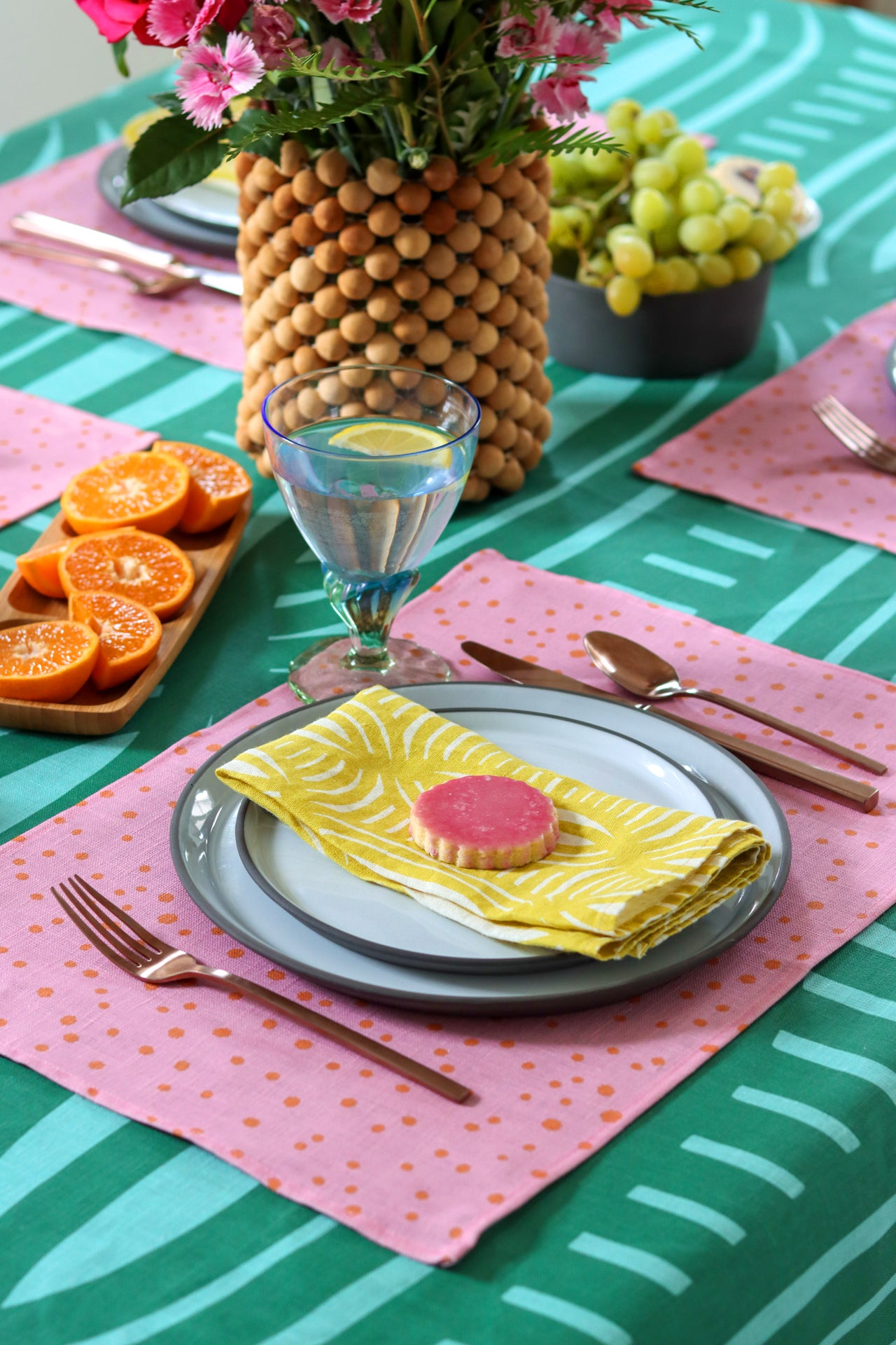 Colorful table setting with yellow napkins, pink polka dot placemats, over a green striped tablecloth. Designed by artist Leila Simon Hayes.