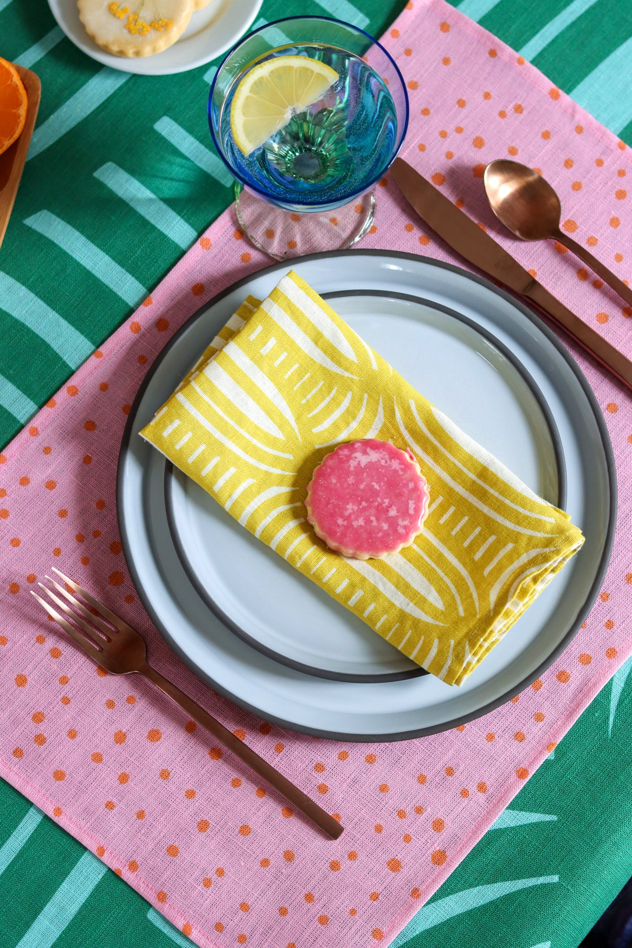 Decorative table setting, yellow patterned napkin, pink polka dot placemat and green striped tablecloth. Designed by artist Leila Simon Hayes