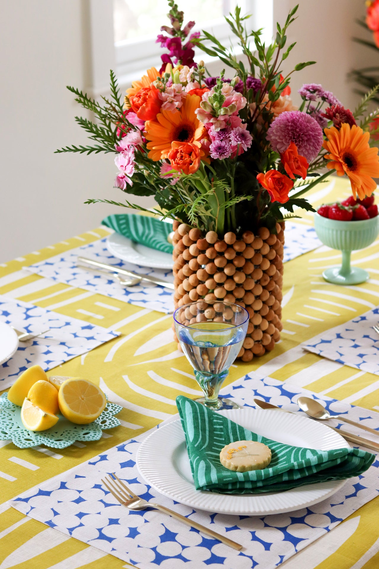 Colorful table setting with green napkins, blue and white dot patterned placemats, and a yellow geometric striped tablecloth.