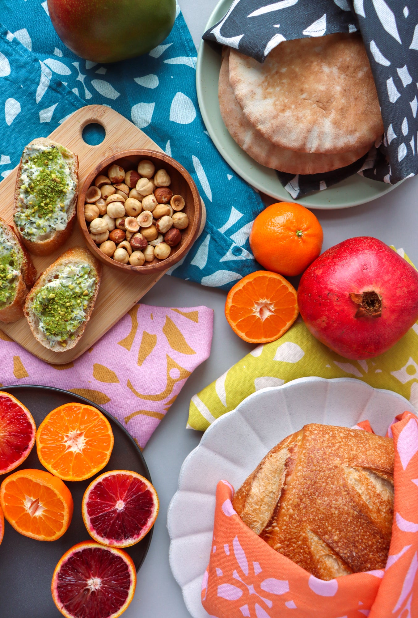 Assorted bread, fruits, and nuts on a colorful tablecloth. Designed by artist Leila Simon Hayes.