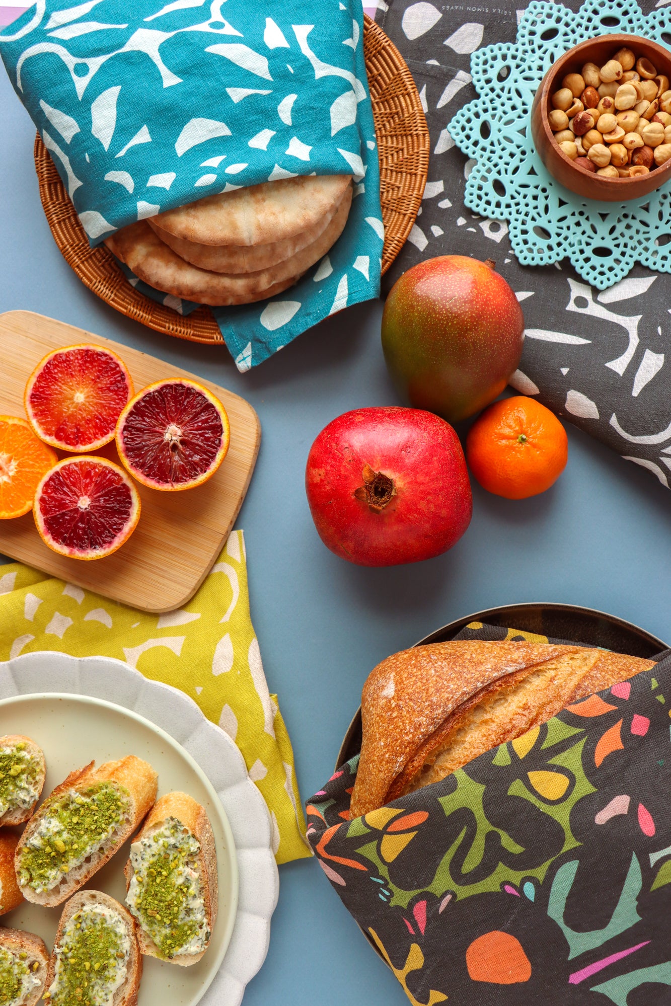 Assorted food items including bread, fruits, and sandwiches wrapped in colorful tea towels. Designed by artist Leila Simon Hayes.